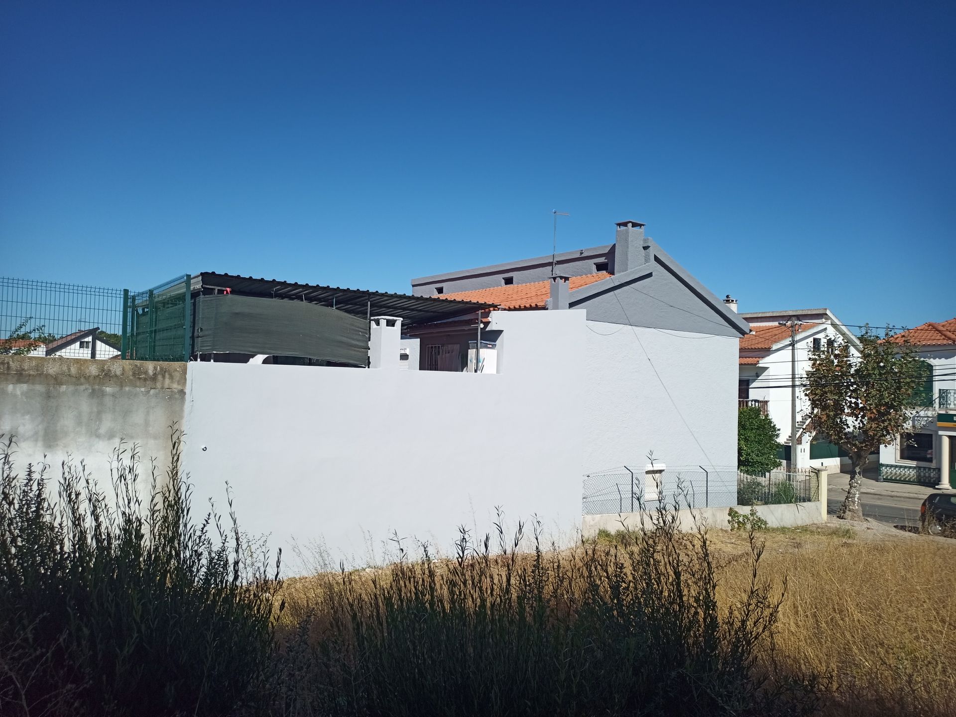 Um edifício cinza claro com telhado escuro contra um céu azul límpido, visto de um campo de vegetação seca.