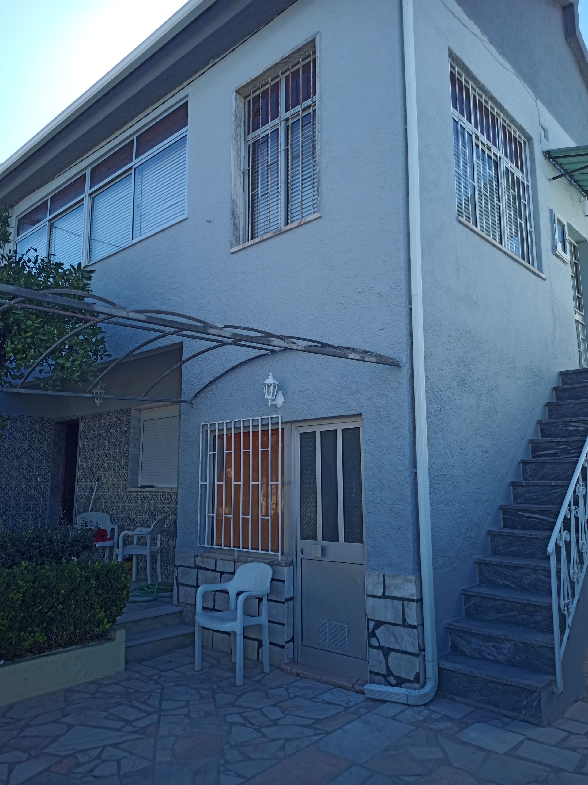 Prédio de dois andares em estuque azul claro com detalhes em pedra cinza, escadas e grades de segurança nas janelas.