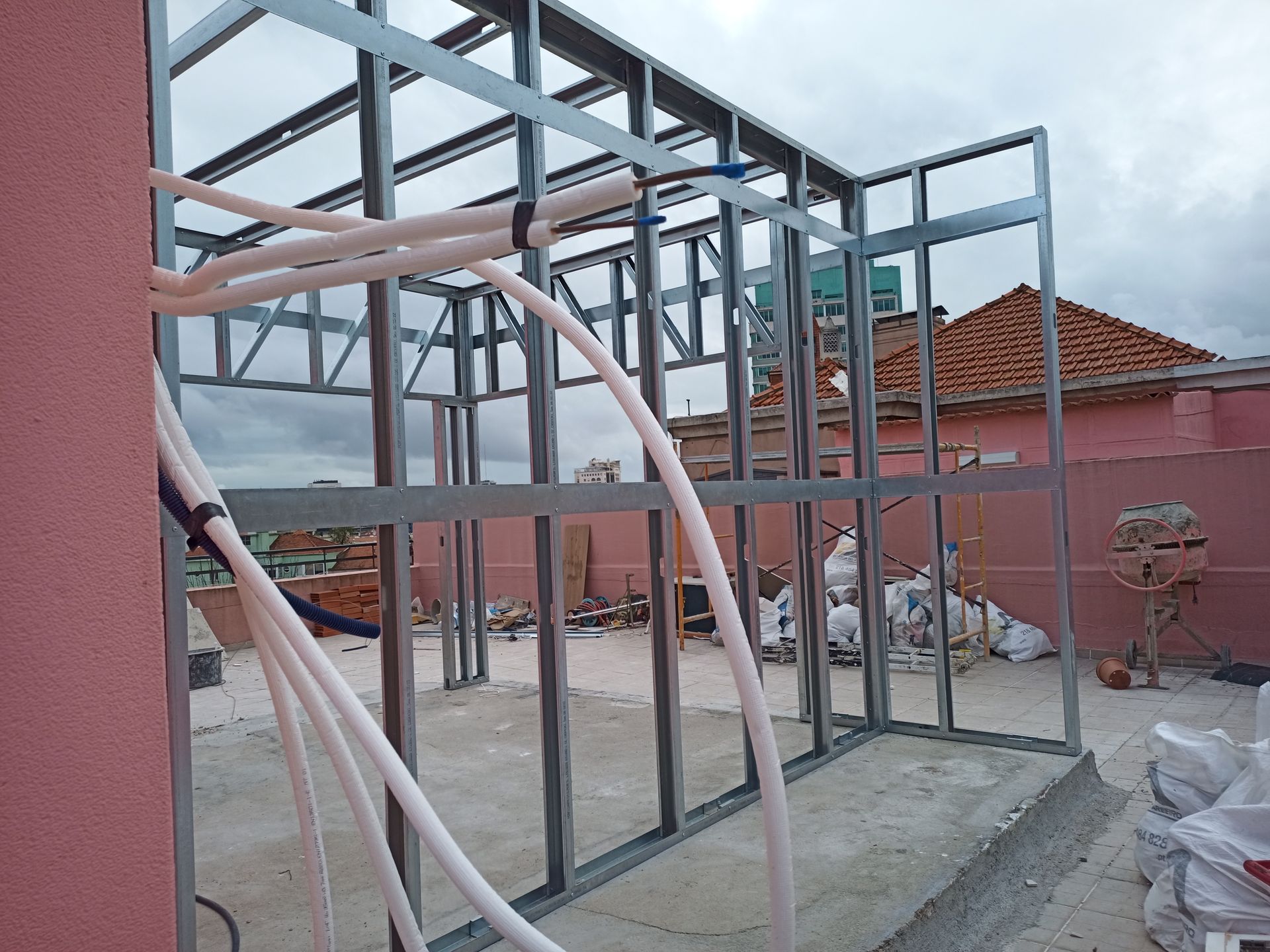 Estrutura metálica de um edifício com tubos brancos acoplados, em contraste com uma parede e telhado rosa.