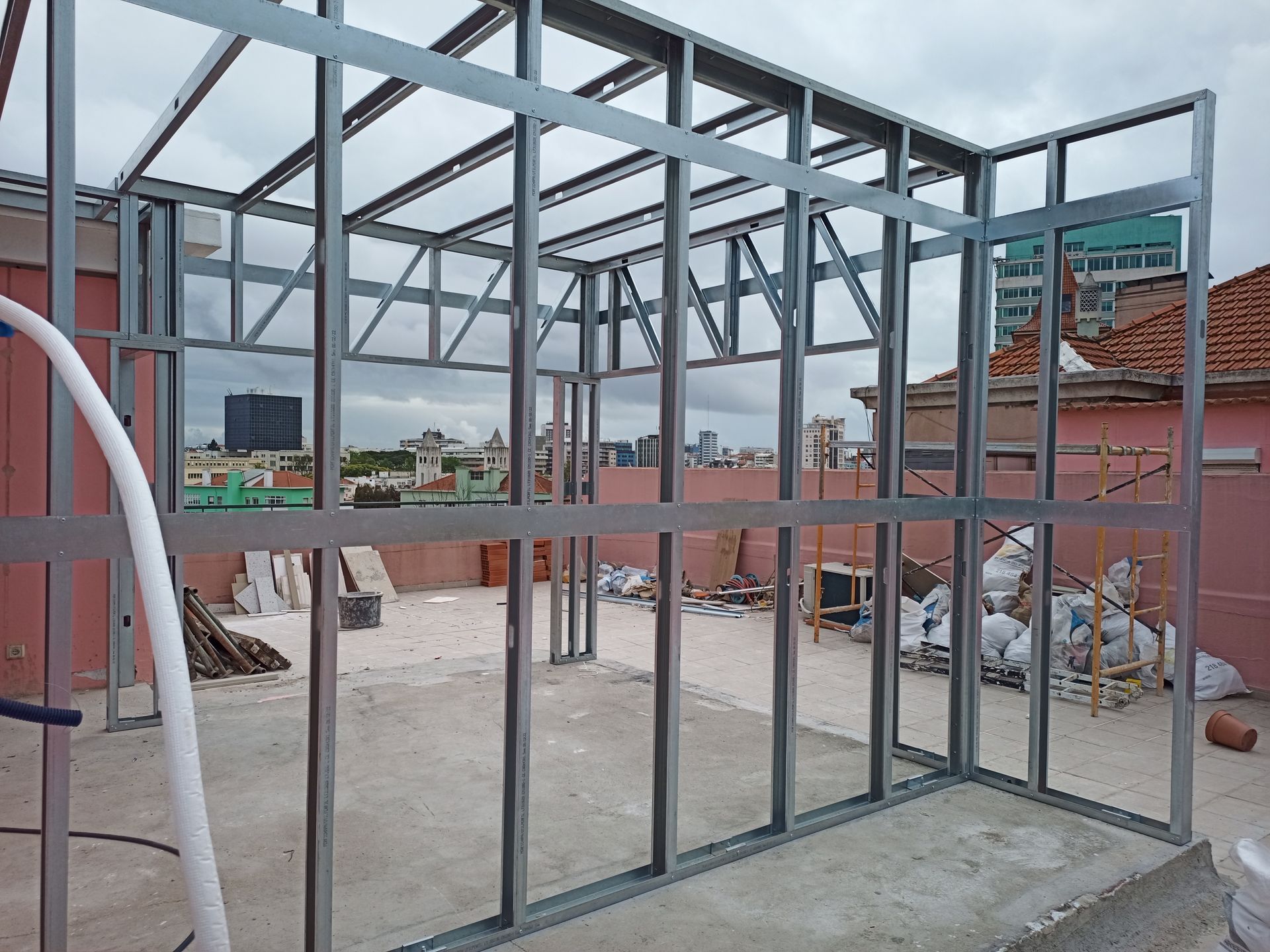 Estrutura metálica de um cômodo em construção em um terraço, tendo como pano de fundo a área urbana.
