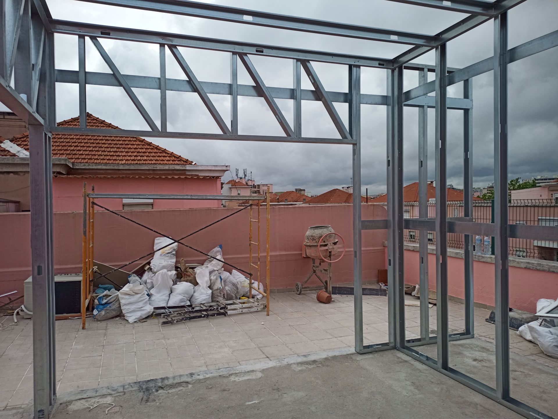 Estrutura metálica em um telhado com céu nublado ao fundo. Materiais de construção e andaimes estão presentes.