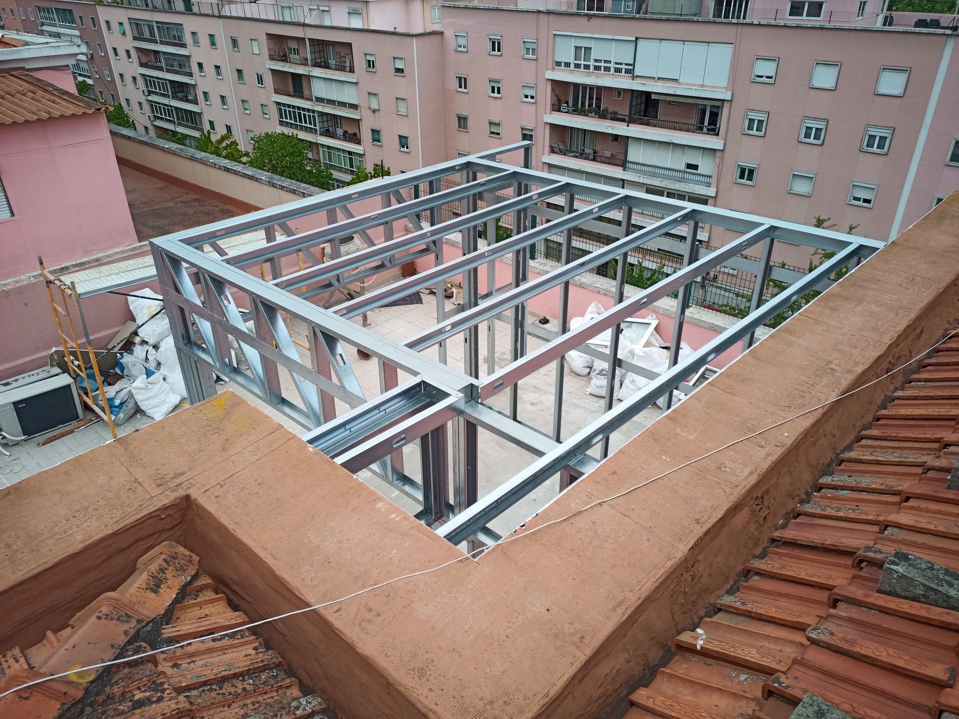 Estrutura metálica em construção em um telhado, com edifícios ao redor.