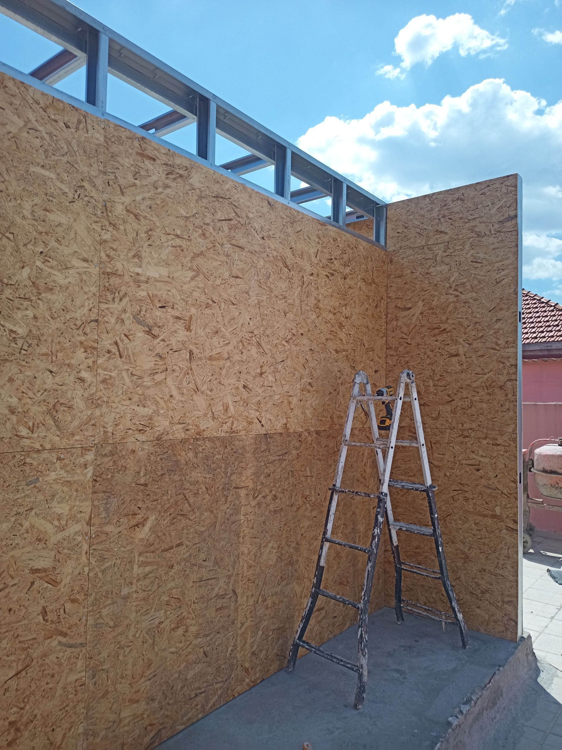 Paredes de OSB em construção com estrutura metálica, escada e céu azul.