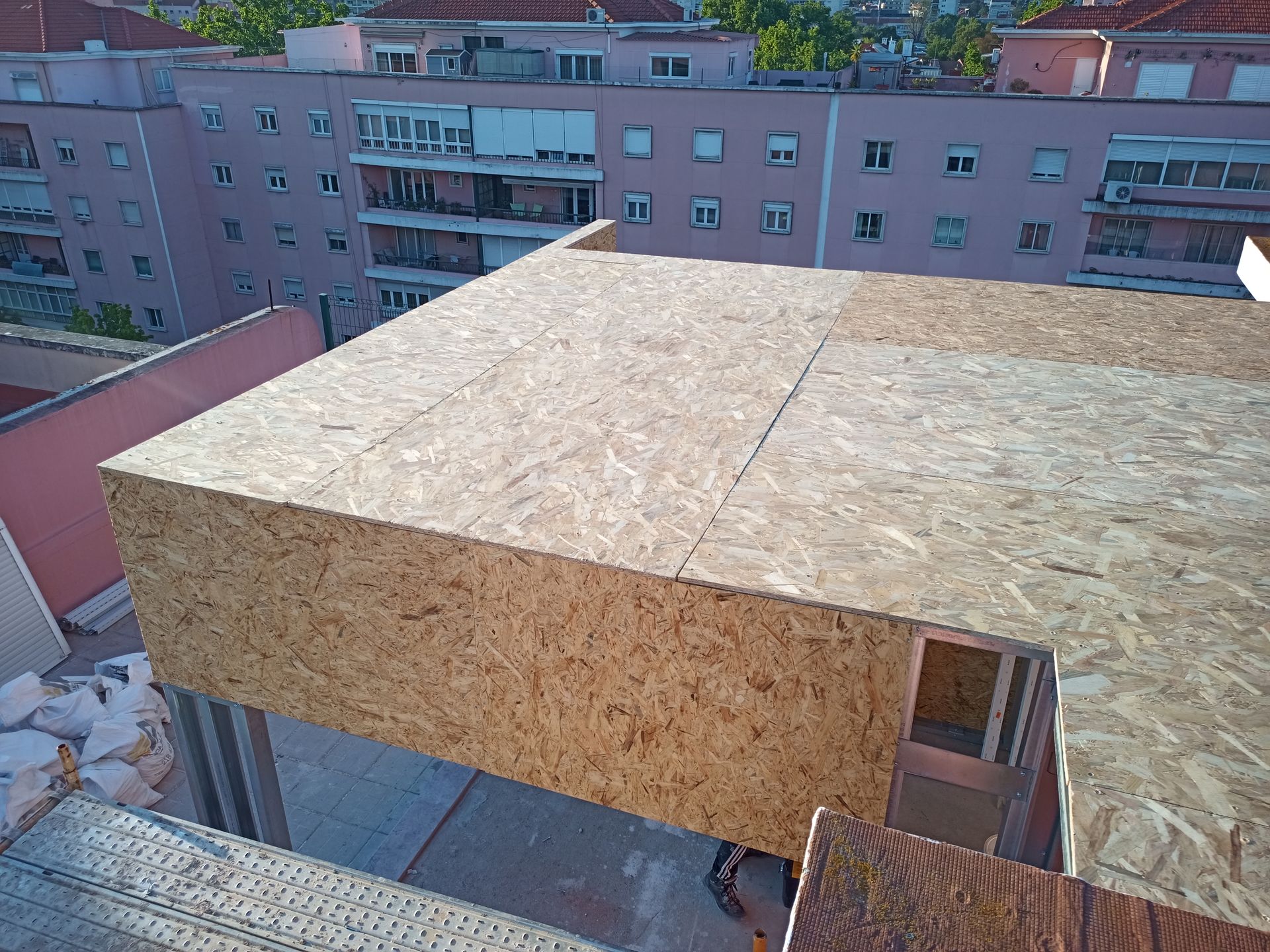 Projeto de construção em cobertura: estrutura revestida com OSB em construção, com prédios de apartamentos ao fundo.