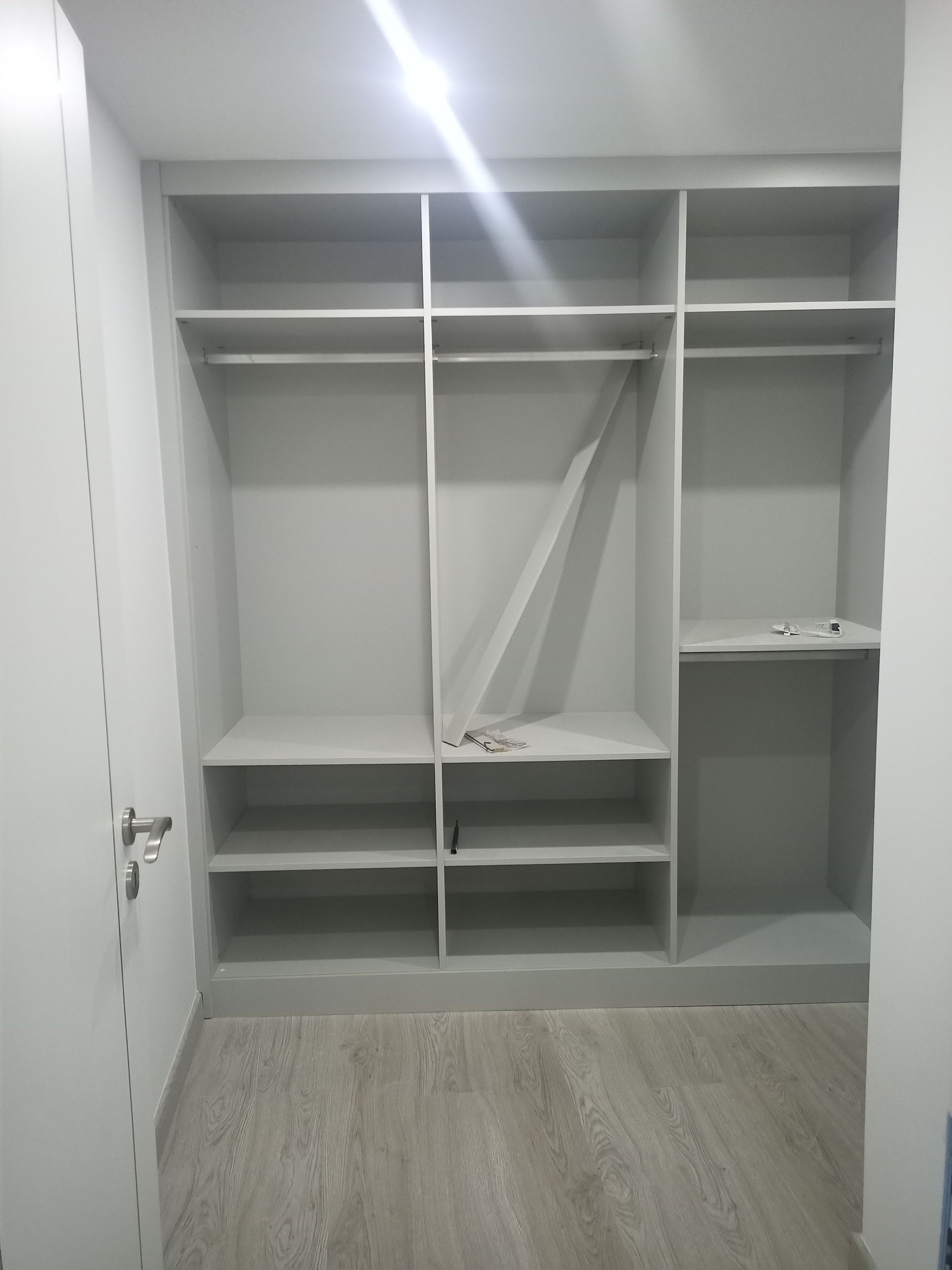 Armário vazio, cinza claro, com prateleiras e varões para pendurar roupas, em um quarto com piso que imita madeira clara.