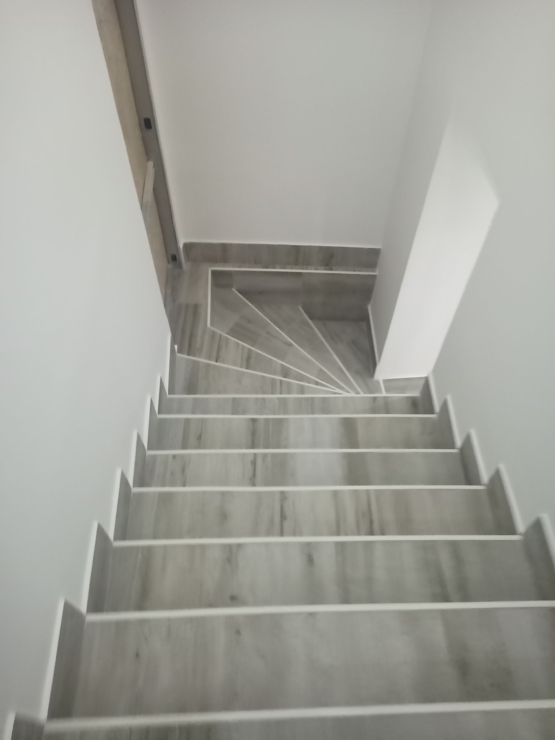 Escadaria com degraus de mármore cinza e detalhes em branco, vista de cima, entre paredes brancas.