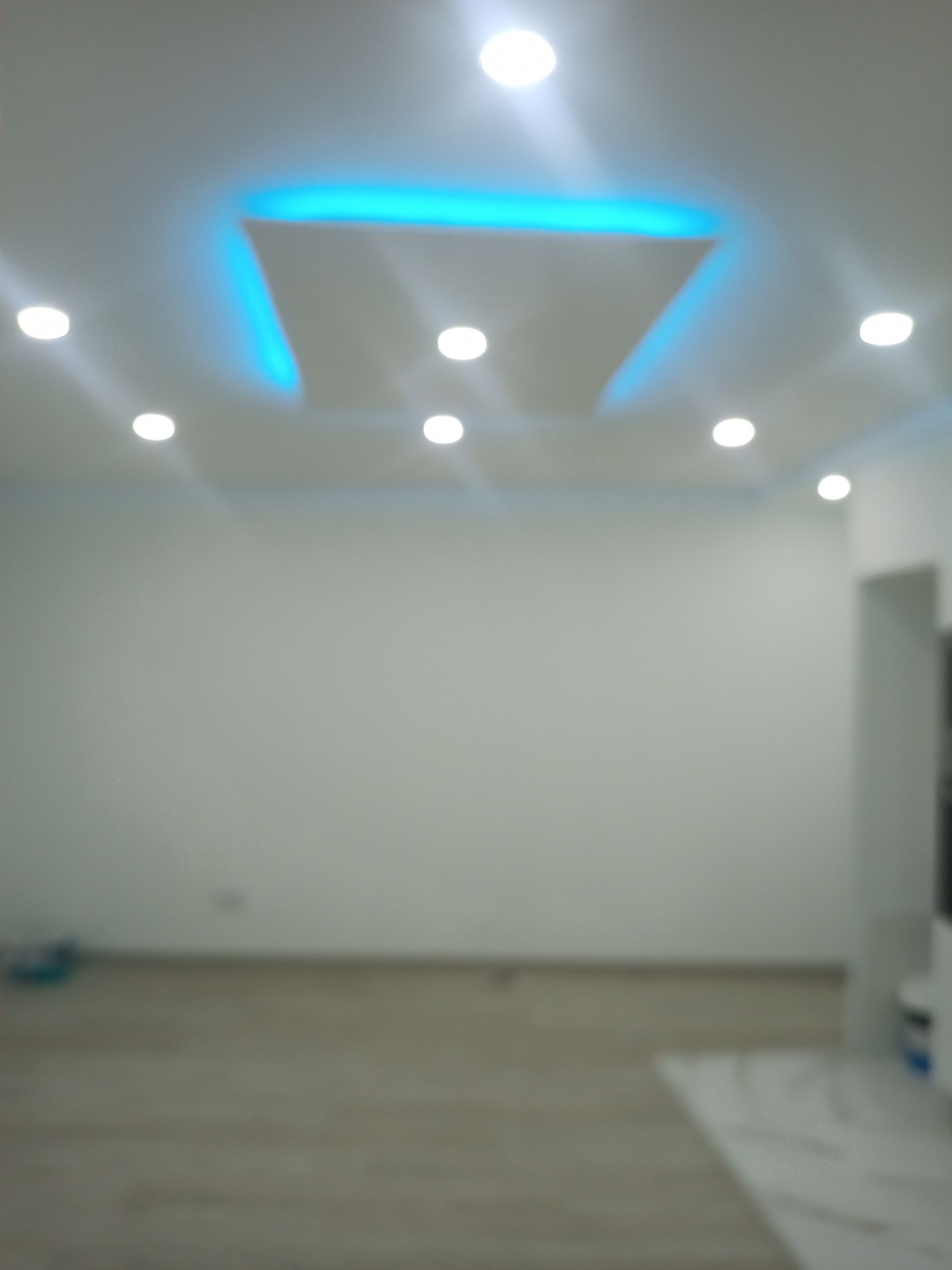 Quarto branco com iluminação embutida, detalhe de luz azul no teto e piso de madeira clara.