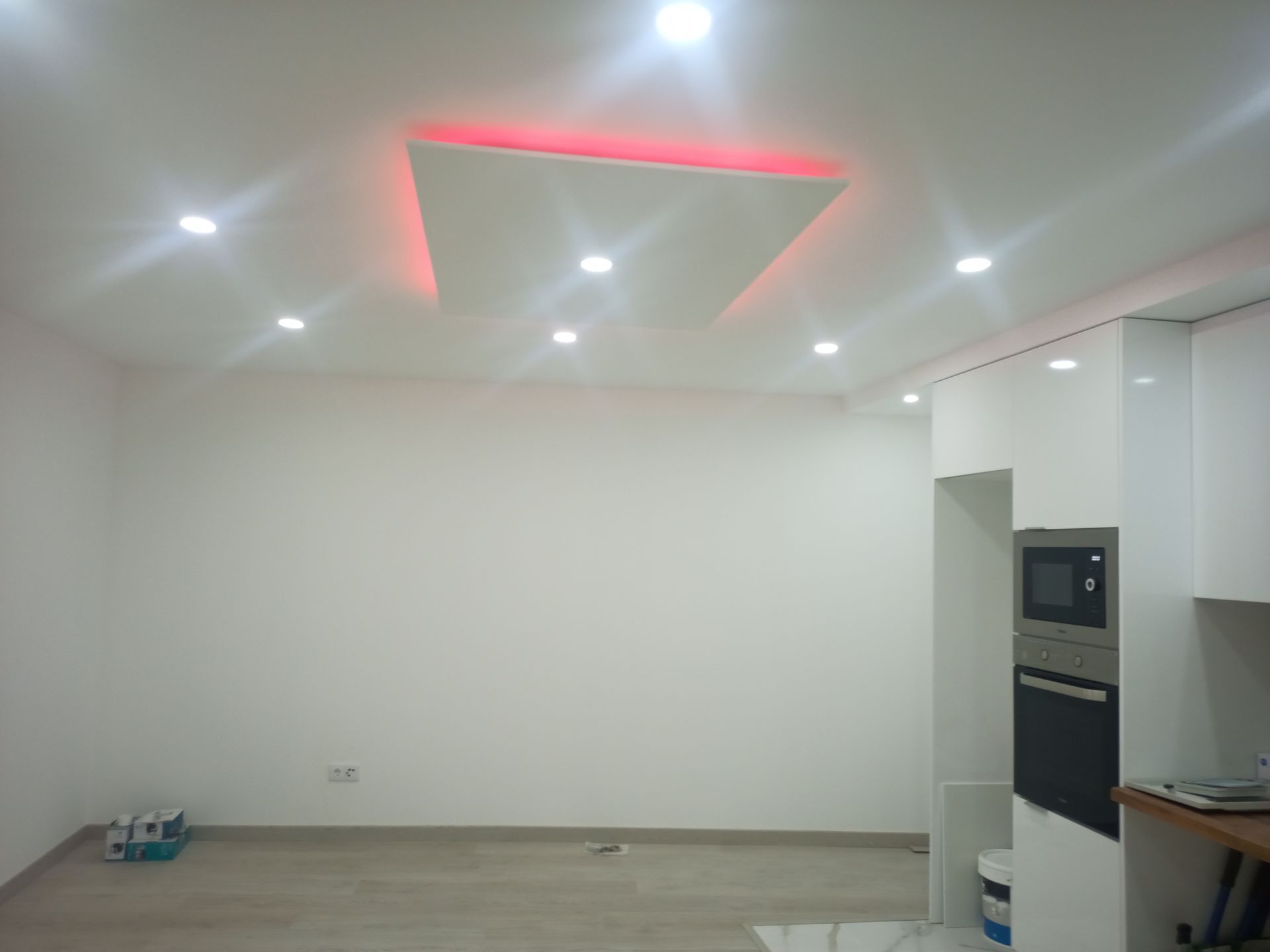 Quarto com interior branco, luzes embutidas no teto, forno embutido, micro-ondas e iluminação ambiente vermelha.