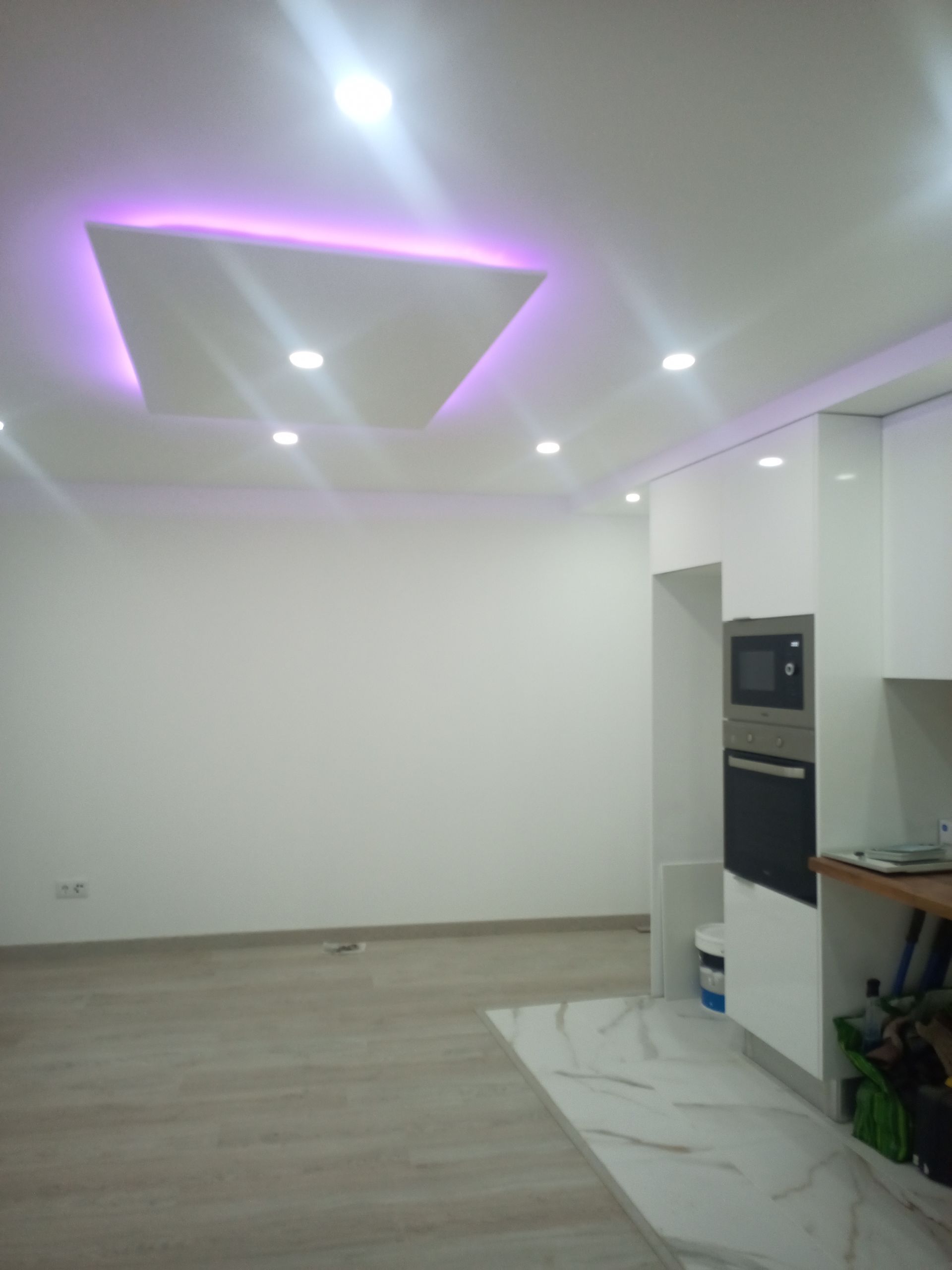 Cozinha moderna branca com luminária geométrica no teto e eletrodomésticos embutidos.