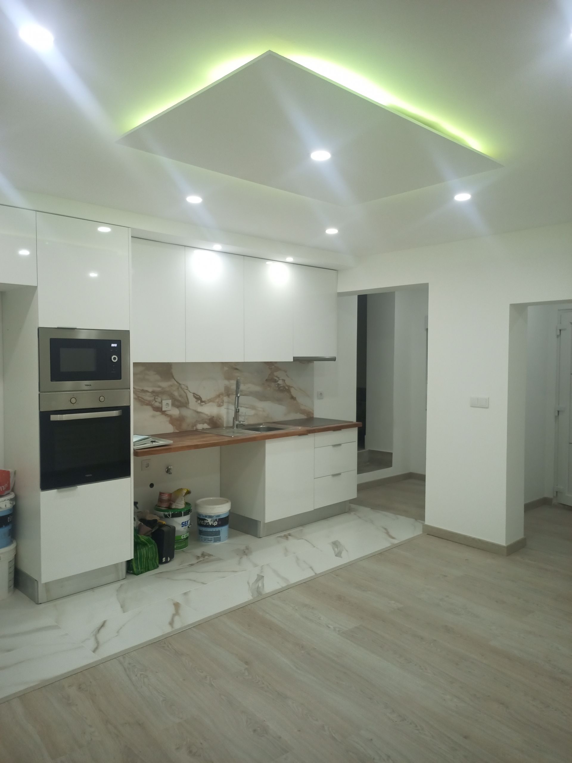 Cozinha branca com eletrodomésticos embutidos e backsplash de mármore; iluminação no teto.