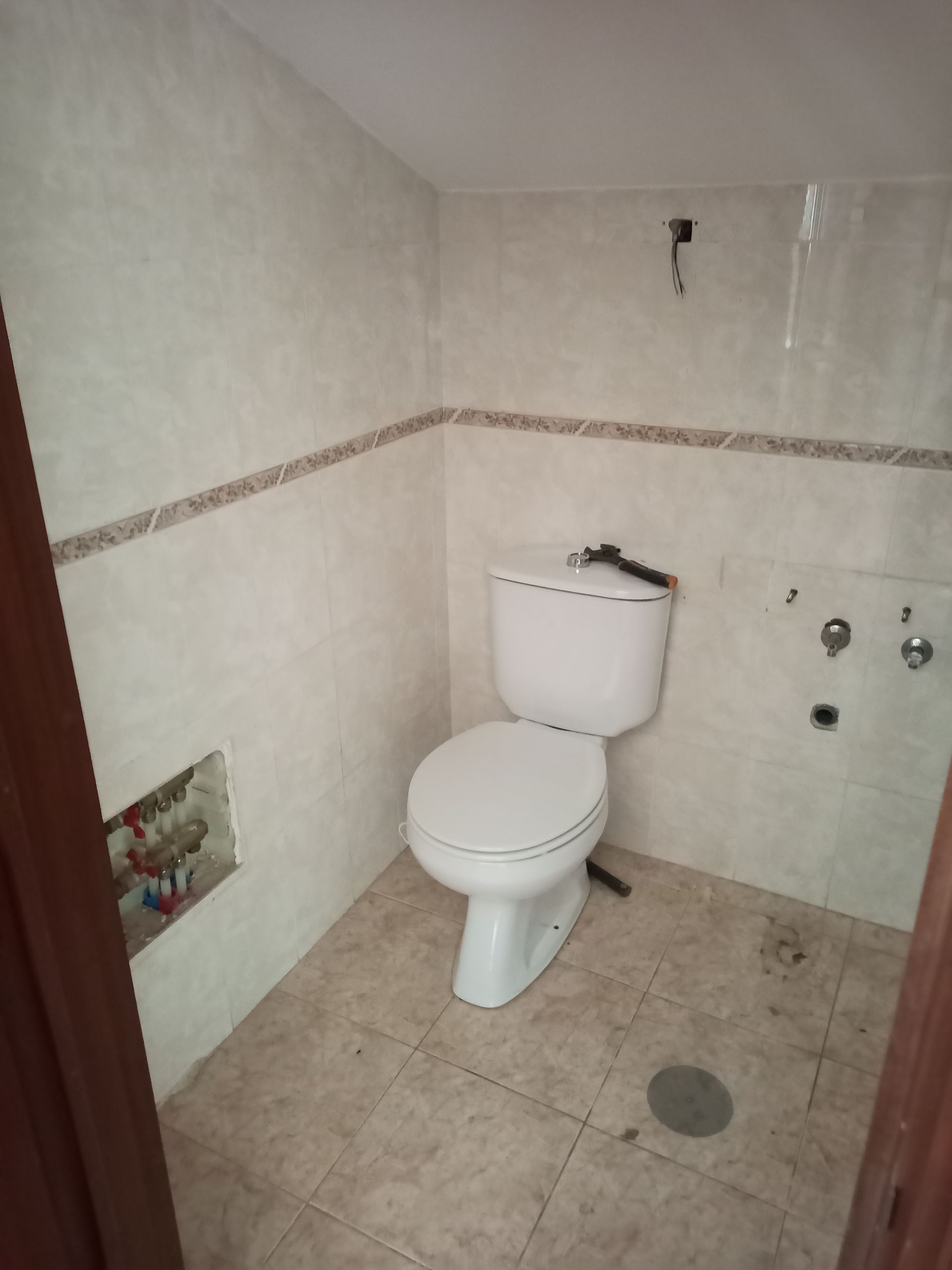 Banheiro pequeno com vaso sanitário branco, paredes e piso revestidos com azulejos bege.