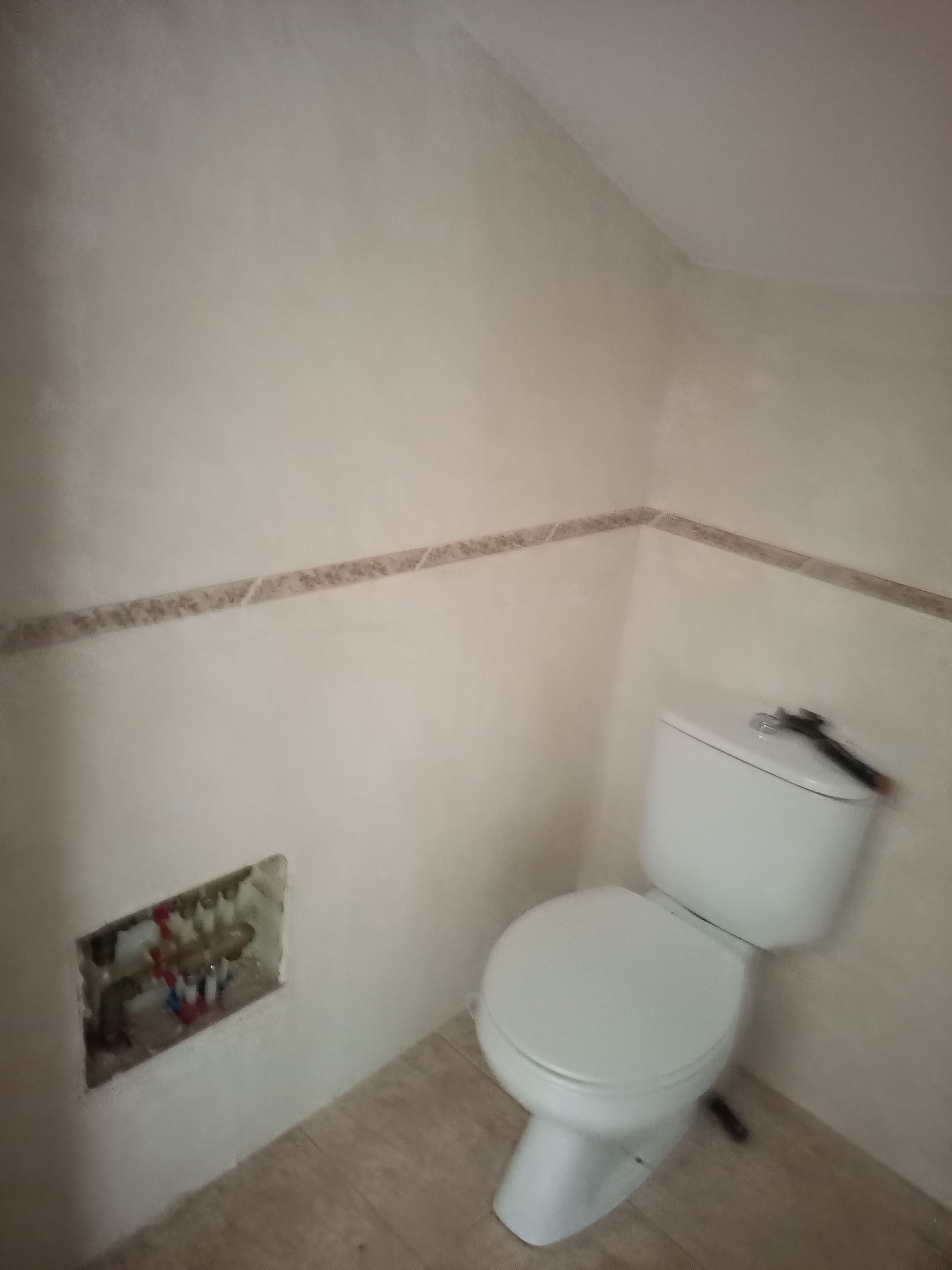 Vaso sanitário em banheiro pequeno com paredes bege, faixa de azulejos e teto inclinado.