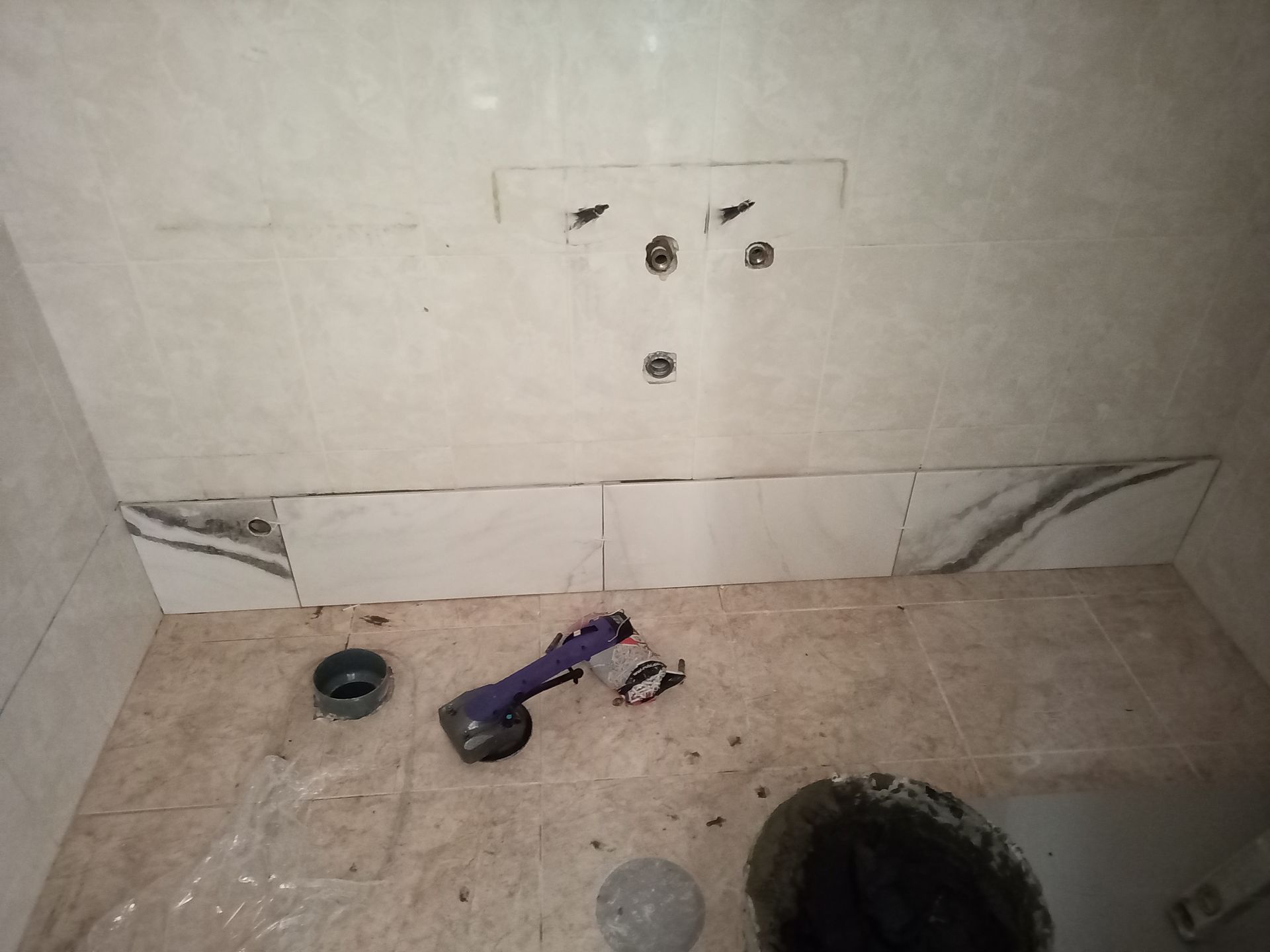 Banheiro em reforma com paredes e piso parcialmente revestidos com azulejos. Instalações hidráulicas aparentes.