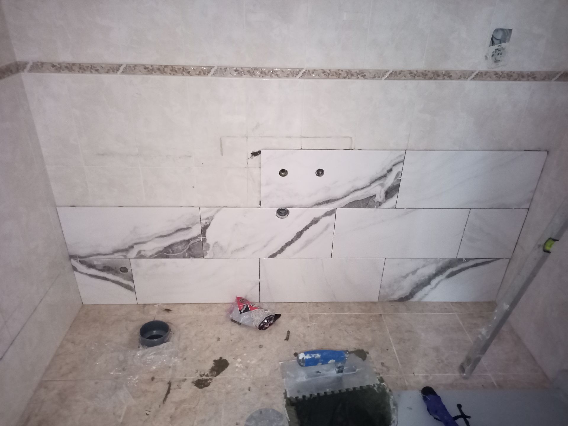 Banheiro com parede parcialmente revestida com azulejos; azulejos com aparência de mármore branco e cinza, acessórios de encanamento.