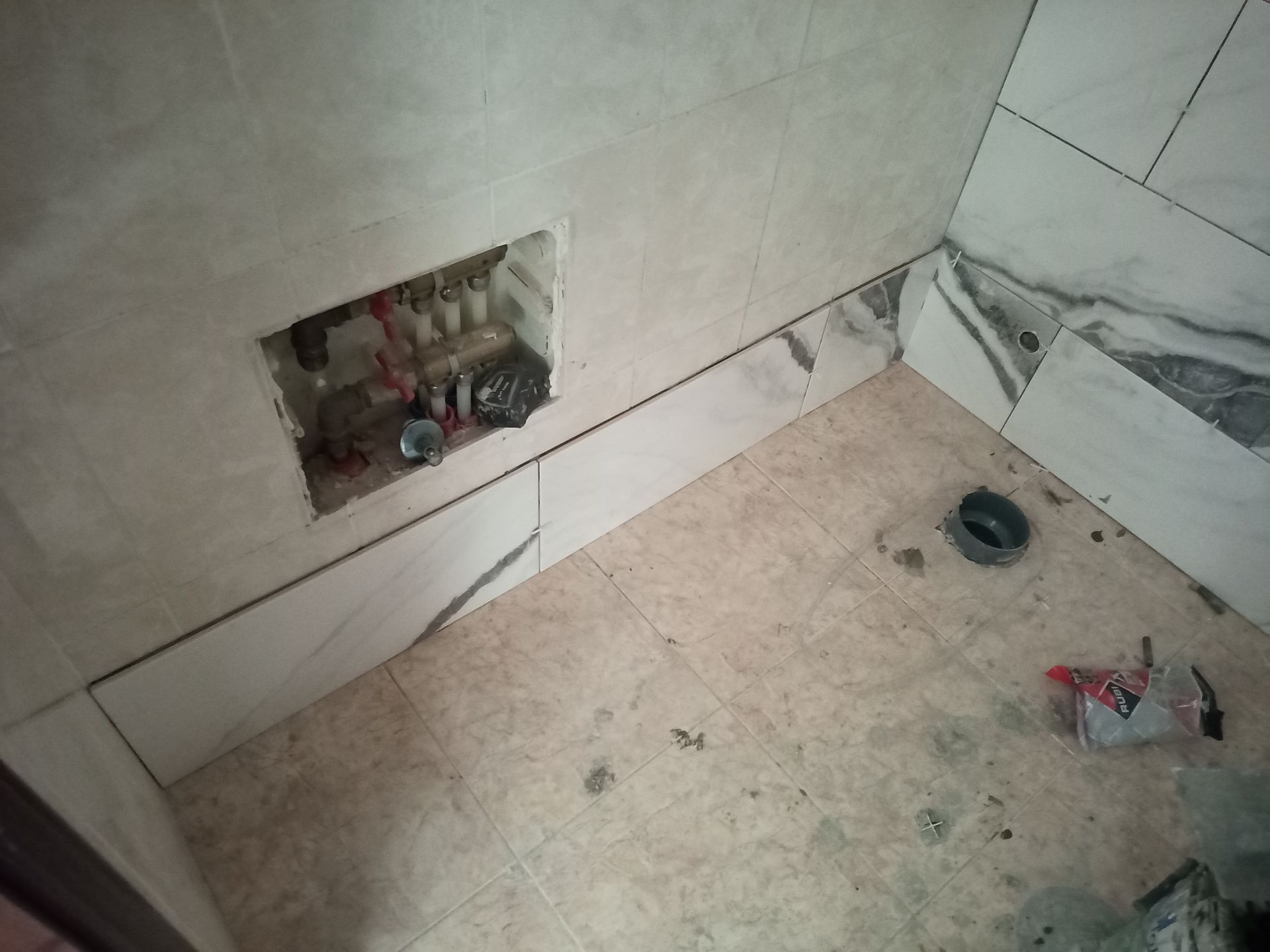 Banheiro em construção com paredes e piso revestidos com azulejos, além de encanamento embutido.