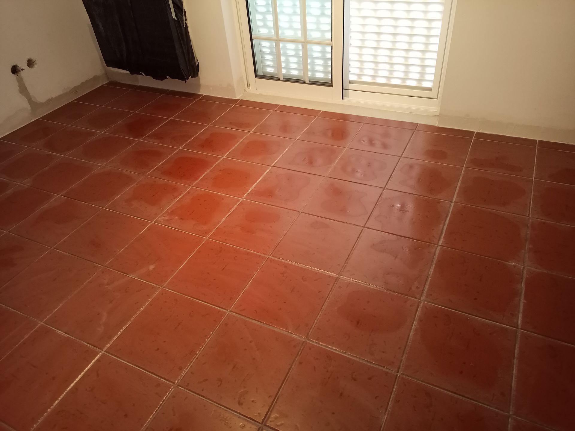 Piso de ladrilho vermelho em um quarto com janela e um radiador escuro.