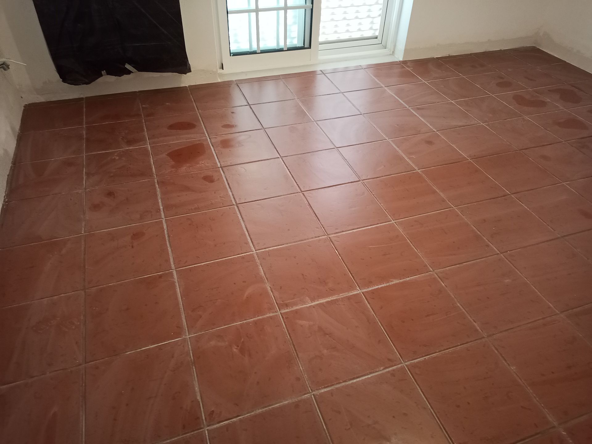 Piso de azulejo marrom em um quarto com janela, com manchas de sujeira visíveis.