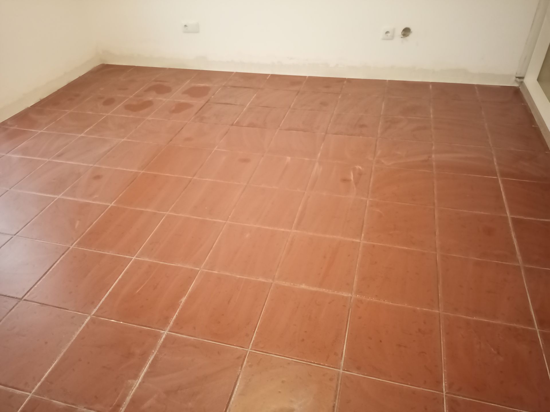Piso de azulejo marrom em um cômodo com paredes brancas, possivelmente um espaço vazio.