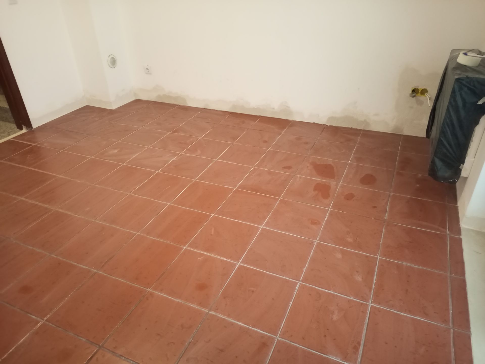 Quarto com piso de ladrilho cor terracota, paredes brancas e algumas manchas de água.