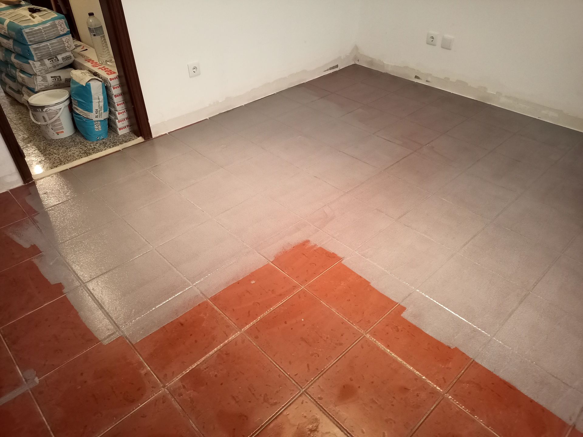 Piso em azulejo: Azulejos vermelhos com transição para azulejos cinza, cômodo parcialmente reformado.