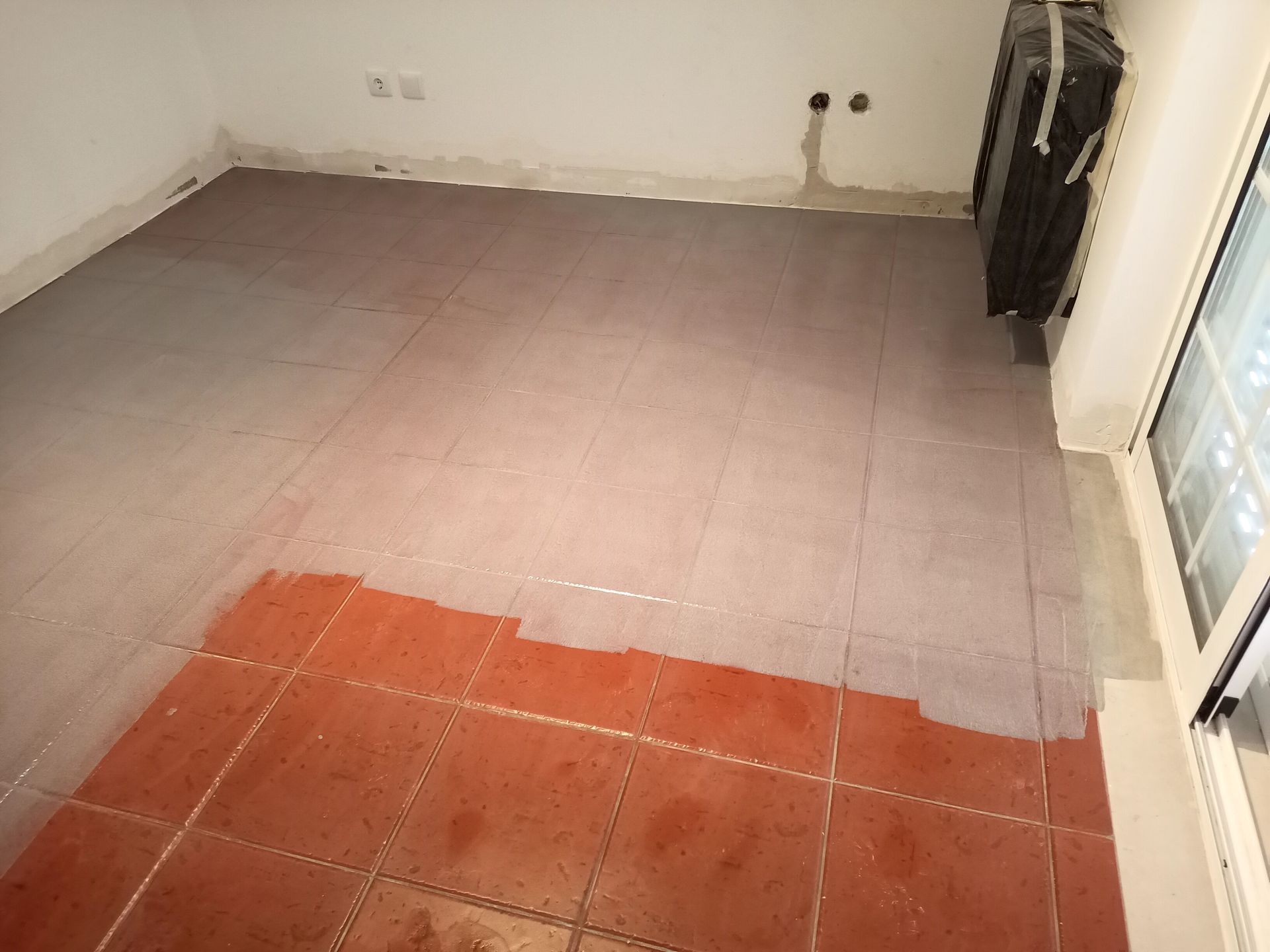 Quarto com piso parcialmente revestido com azulejos. Azulejos vermelhos em primeiro plano, azulejos cinza cobrindo grande parte da área do piso. Paredes brancas.