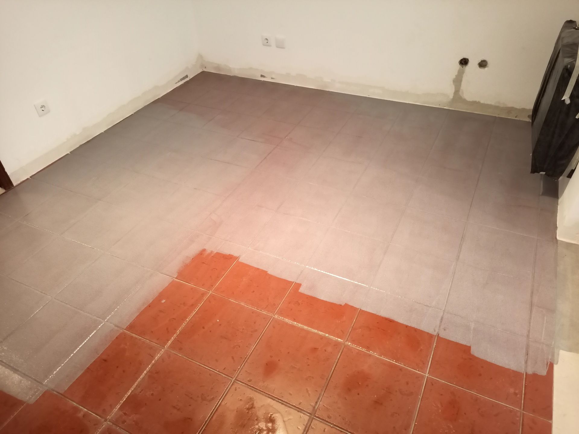 Quarto com piso de ladrilho vermelho sendo pintado de cinza; paredes brancas.