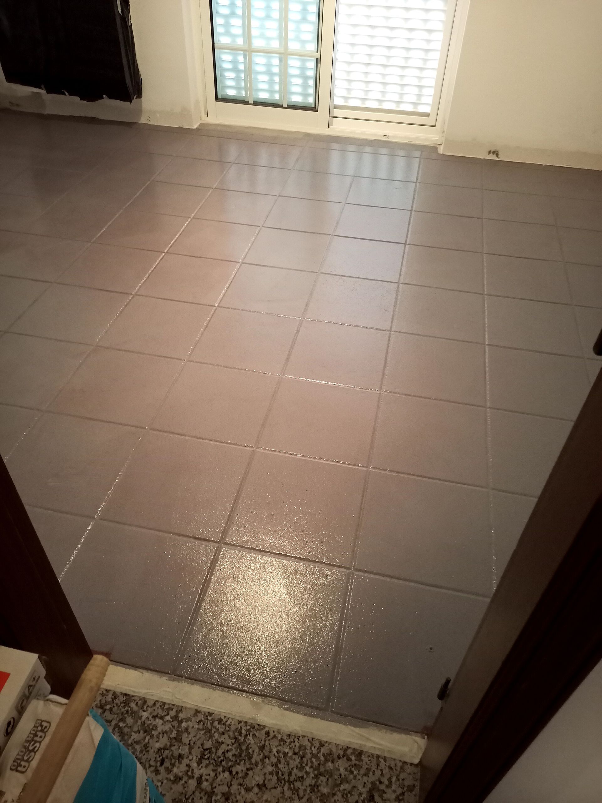 Piso de azulejos cinza com janela, porta e luz refletida em uma superfície molhada.