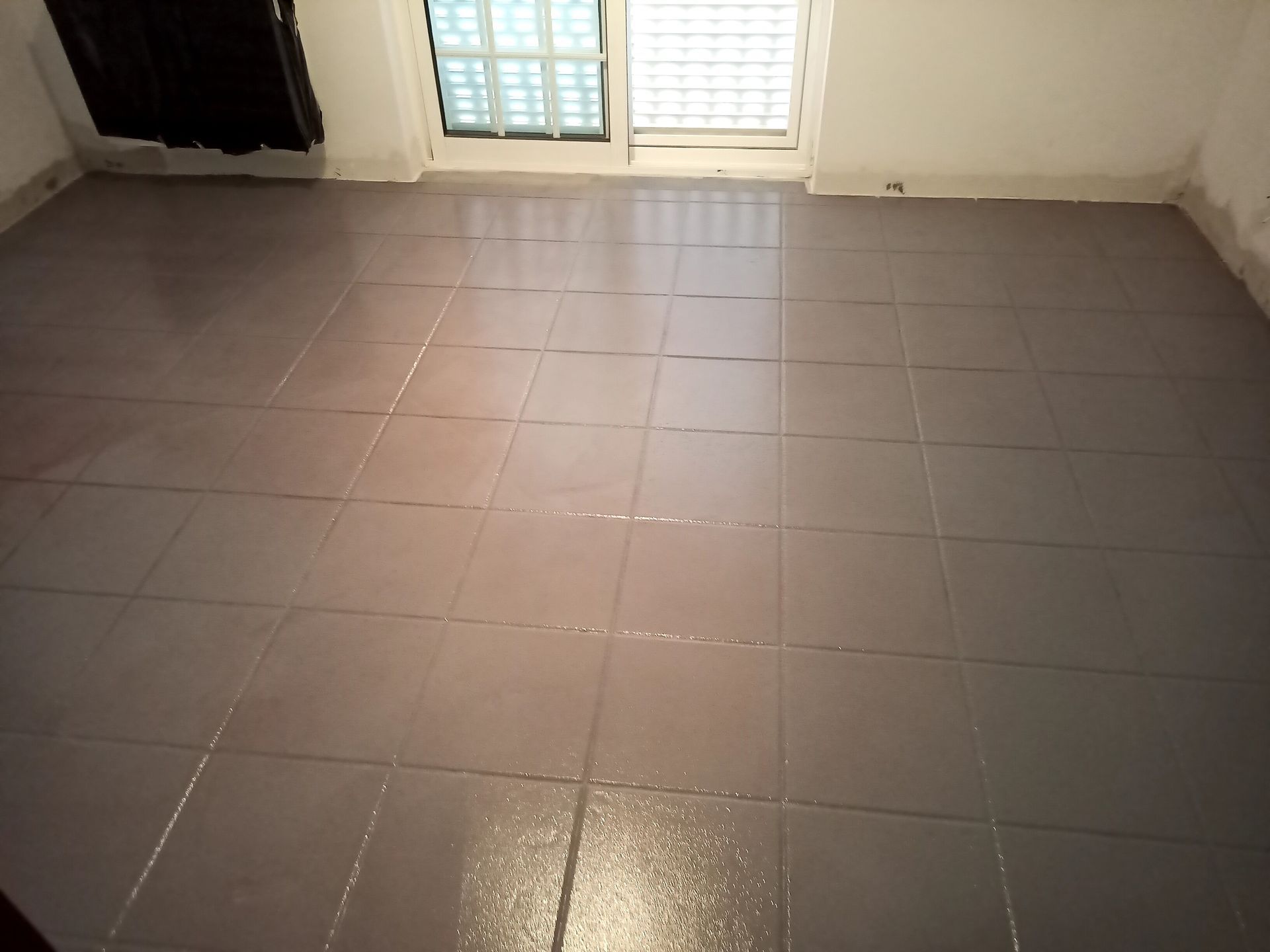 Piso de azulejos cinza em um quarto com janela e paredes brancas.