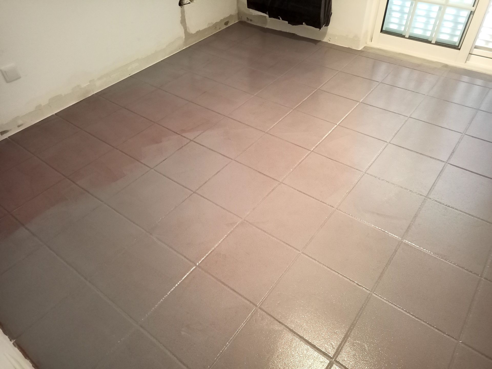 Piso de azulejos cinza recém-rejuntado em um cômodo, com manchas de umidade visíveis.