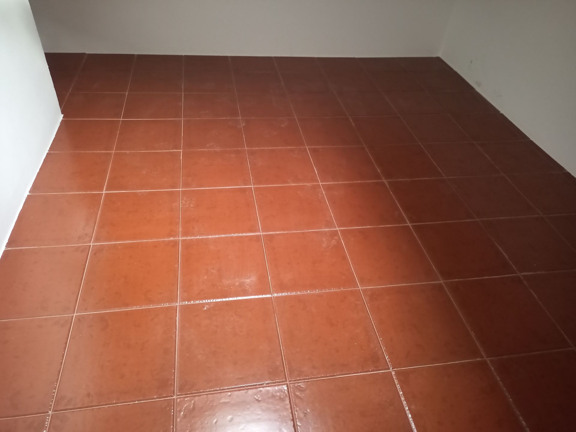 Piso de azulejos marrons em um cômodo vazio, paredes brancas.