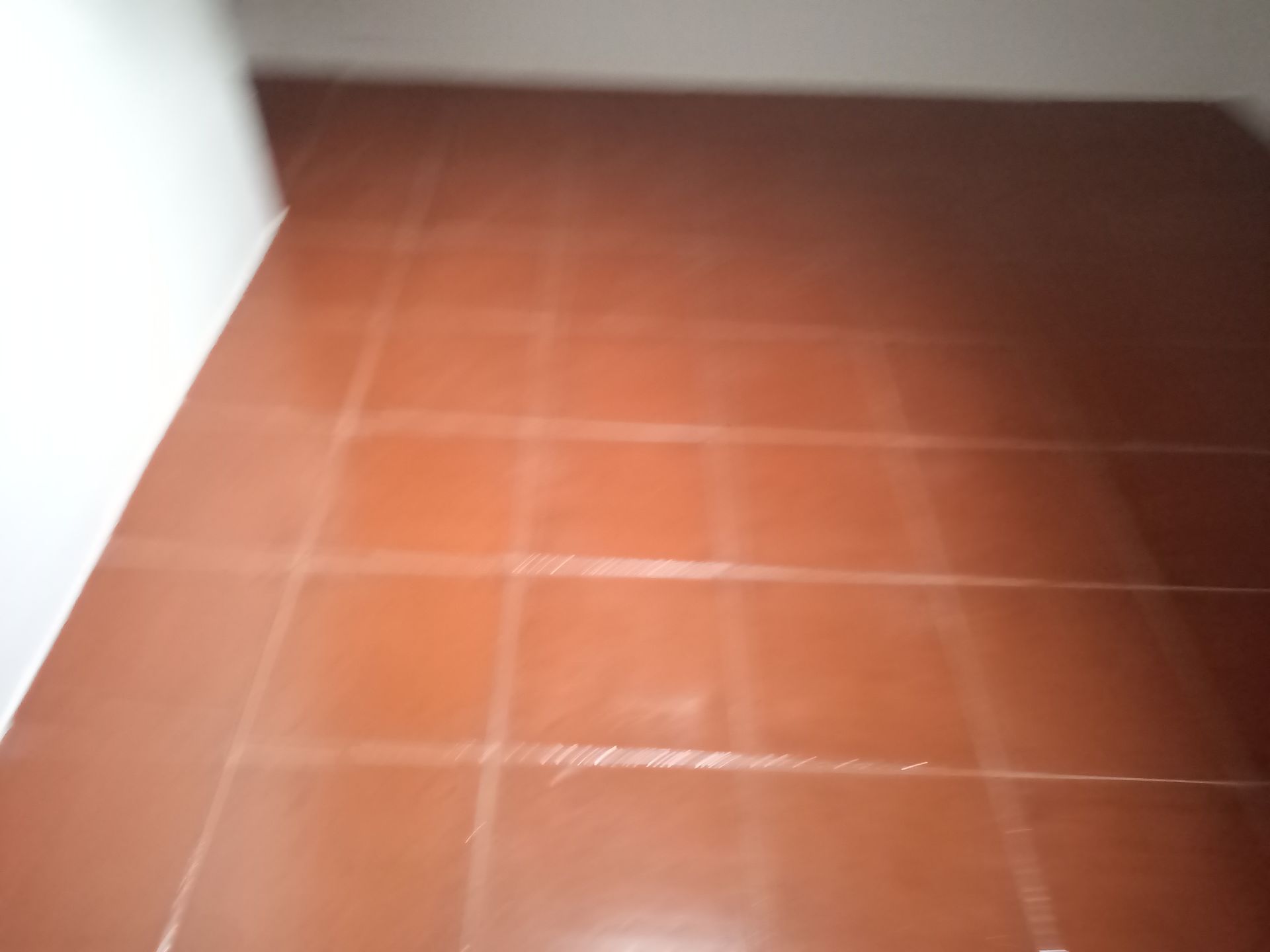 Piso de azulejos marrons em um canto. Os azulejos são quadrados e as paredes são brancas.