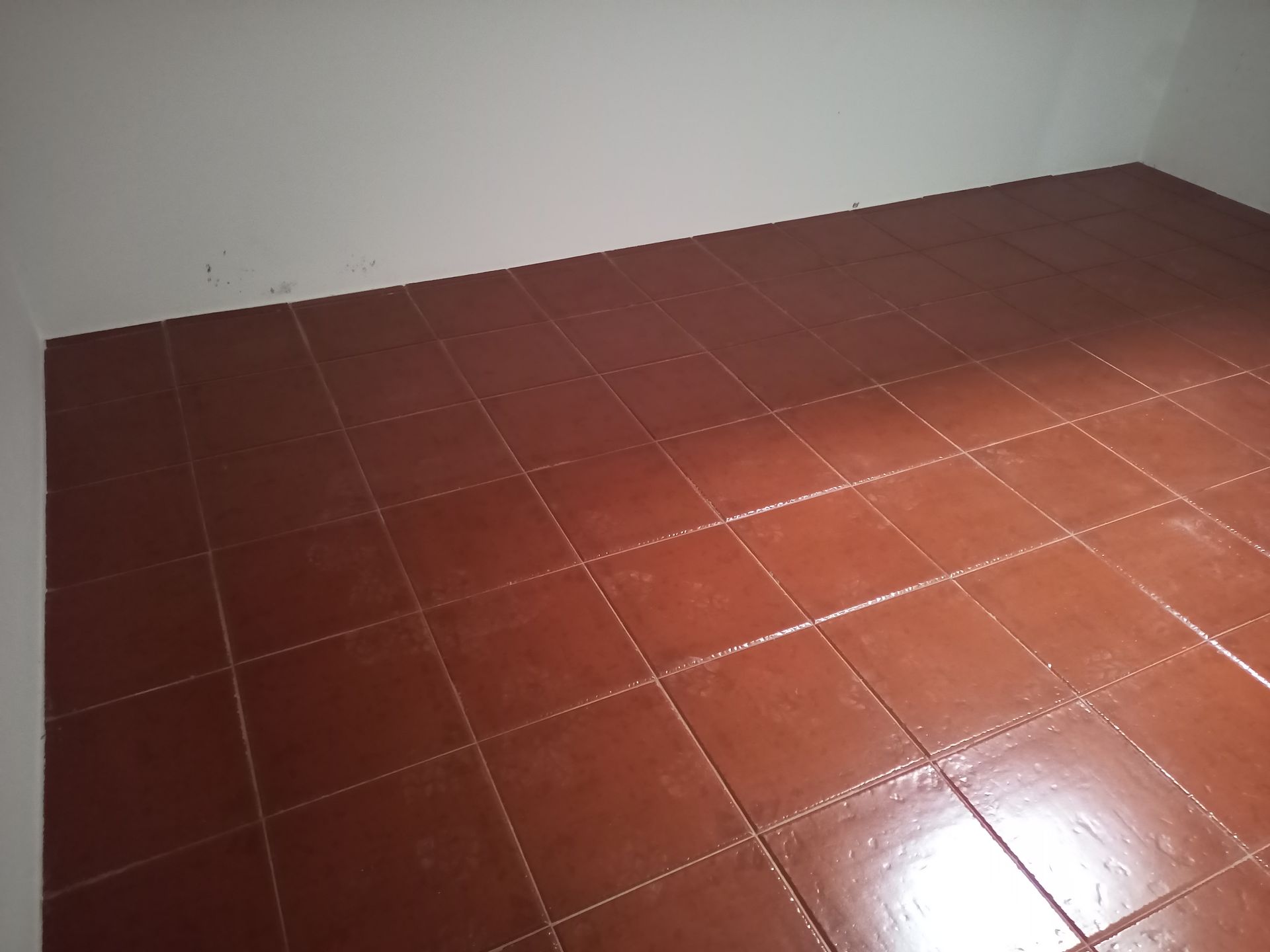 Piso de azulejos marrons em um cômodo vazio, paredes brancas.