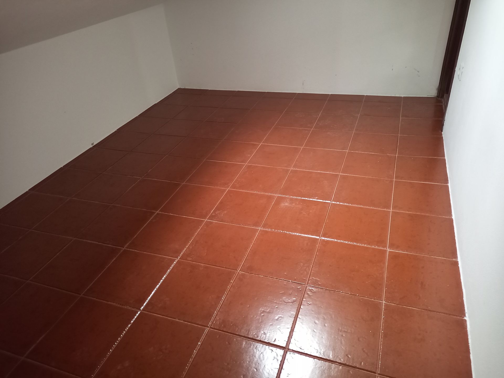 Quarto vazio com piso de azulejos marrons e paredes brancas.