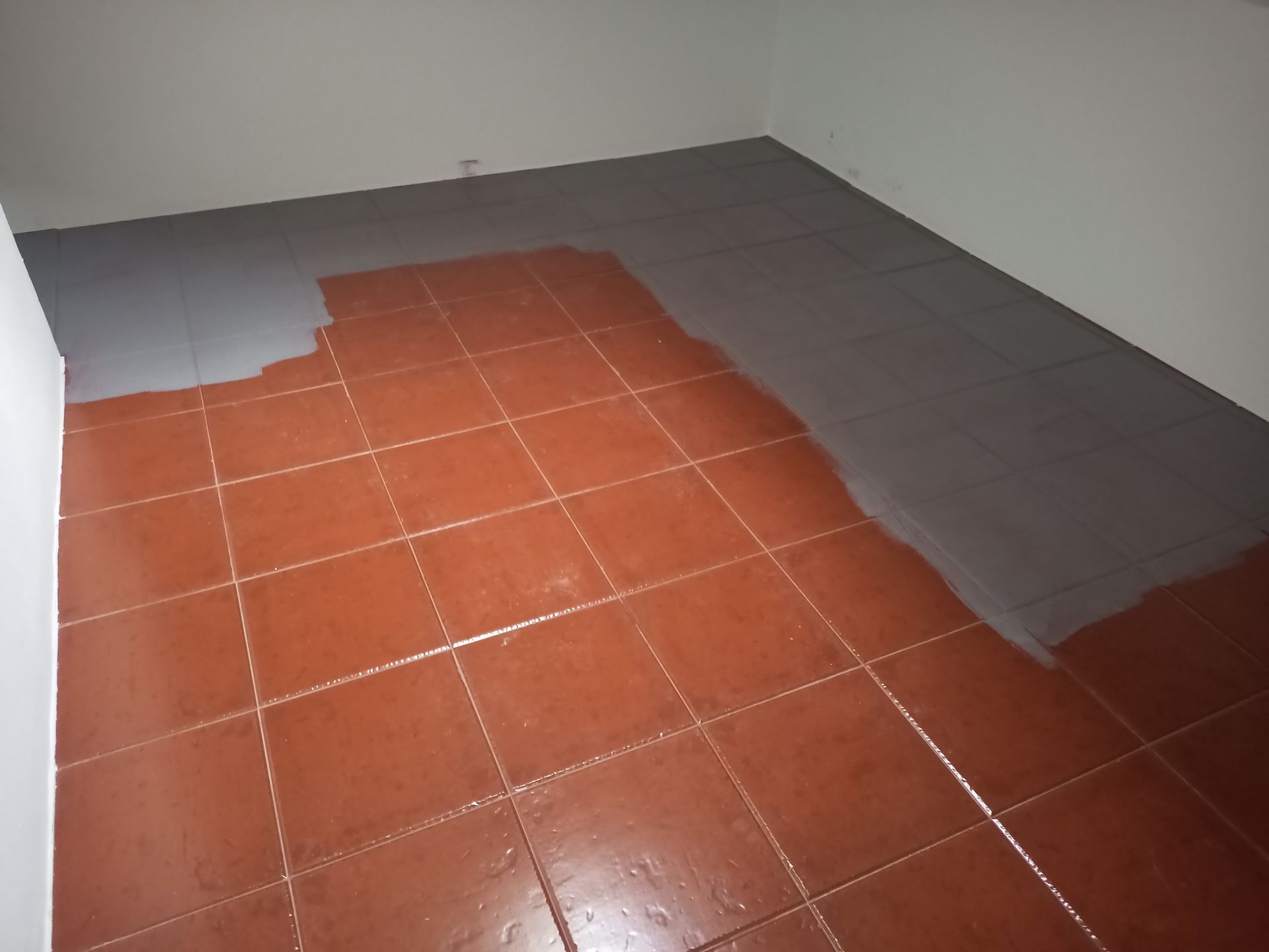 Quarto com piso de ladrilho de terracota parcialmente pintado de cinza. Paredes brancas.
