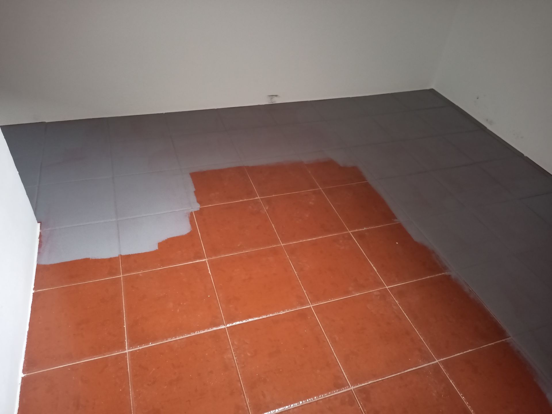 Quarto com piso de ladrilho de terracota parcialmente pintado de cinza.