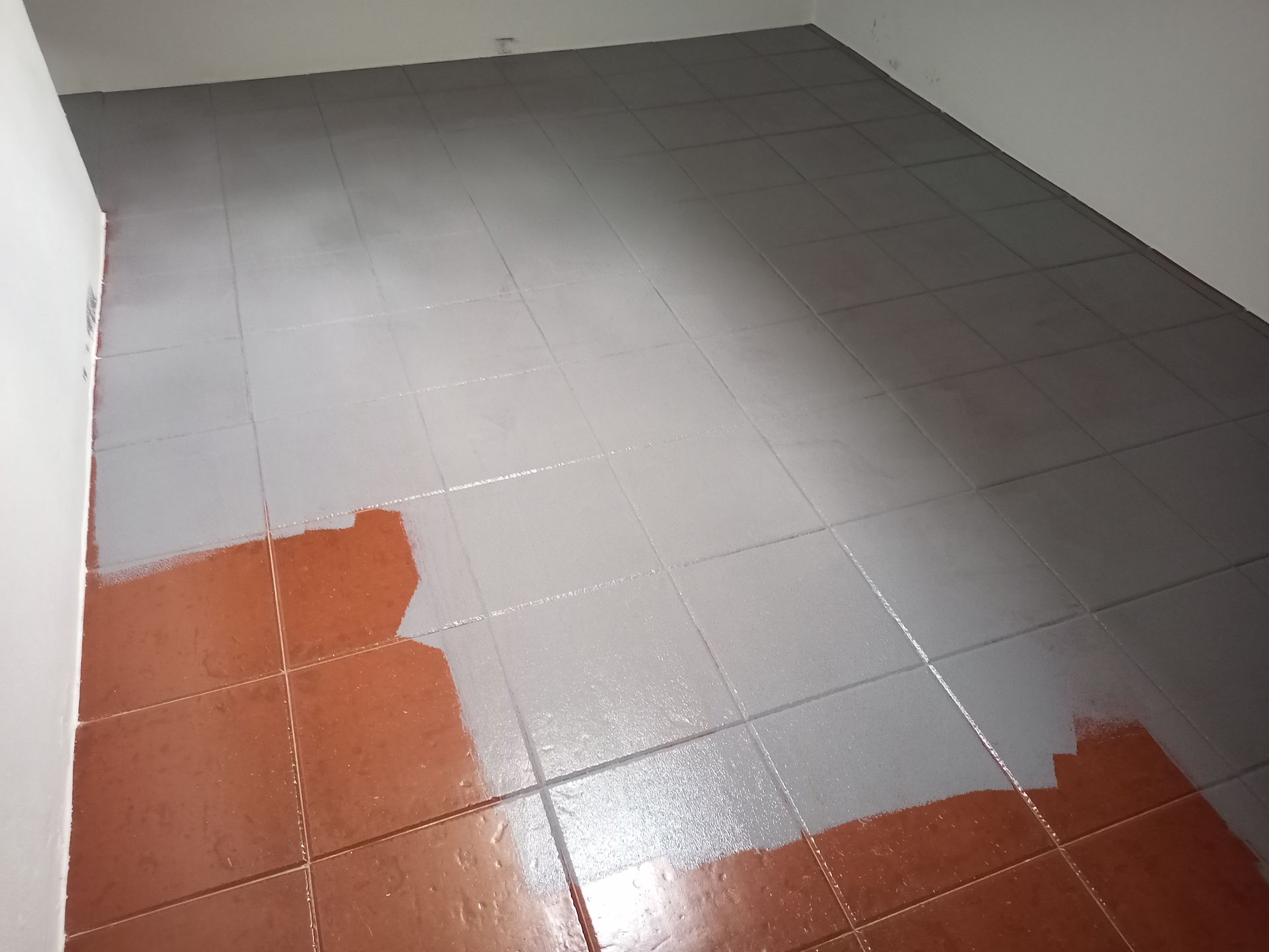 Azulejos no chão, parcialmente pintados de cinza, em uma sala com paredes brancas.
