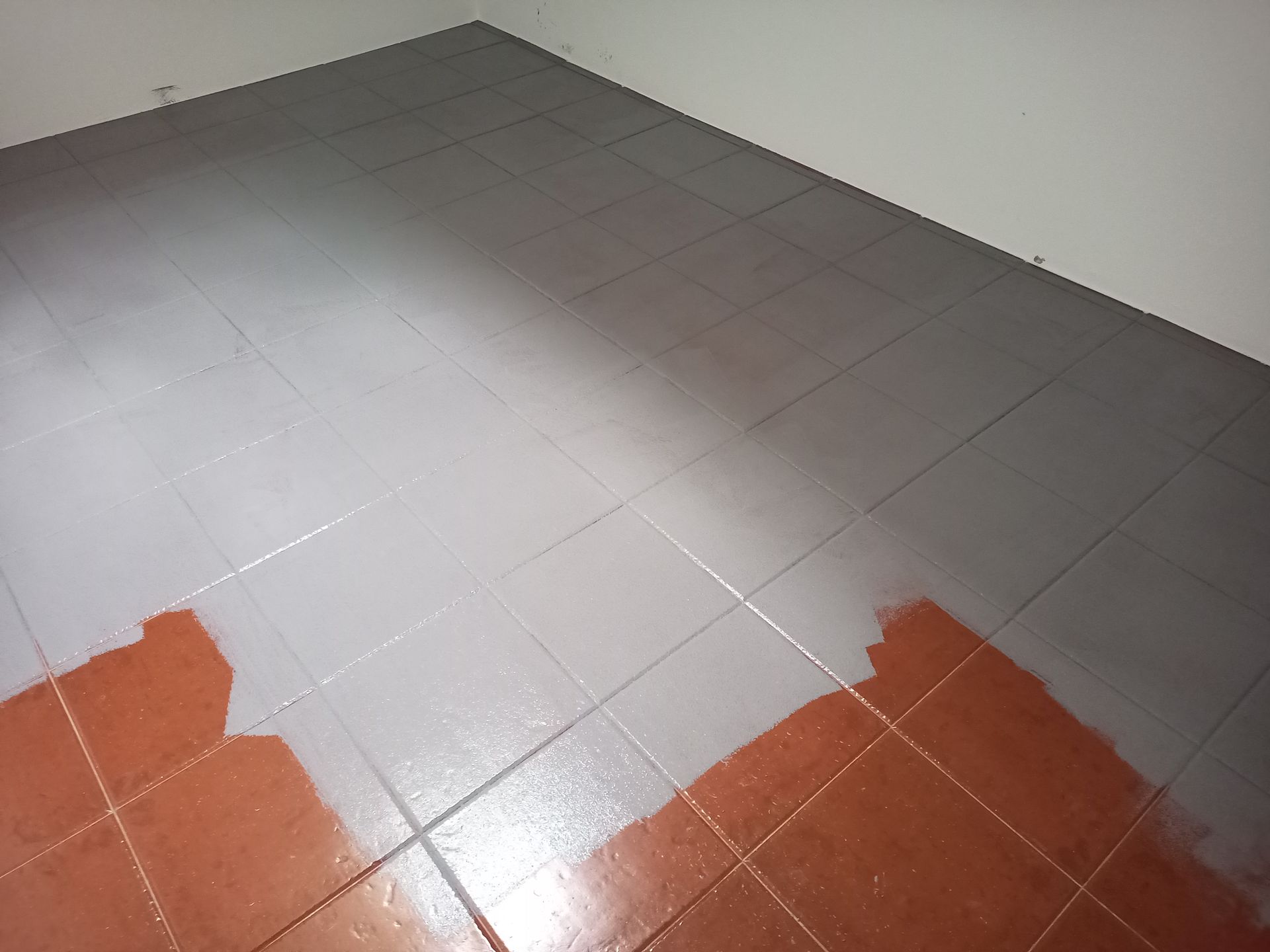 Piso parcialmente pintado de cinza sobre ladrilhos marrons.