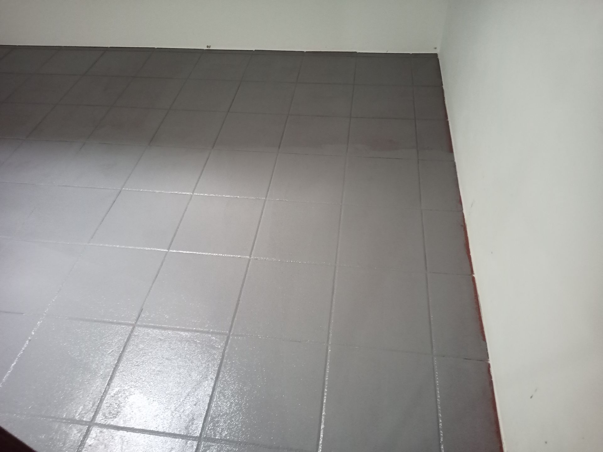 Piso de azulejo pintado de cinza em um cômodo com paredes brancas e detalhes em vermelho visíveis.