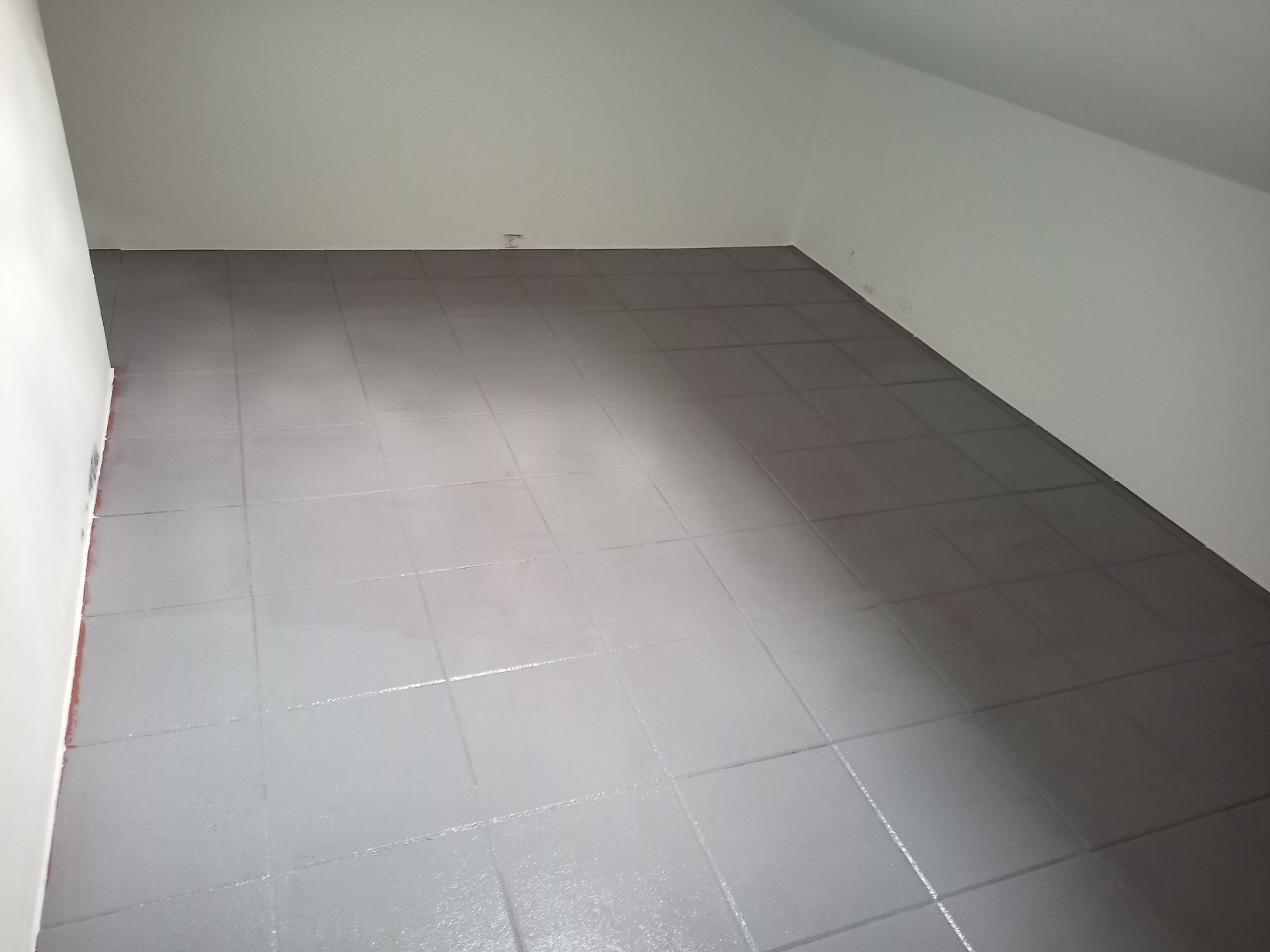 Piso de azulejos cinza em uma sala com paredes brancas e teto inclinado.