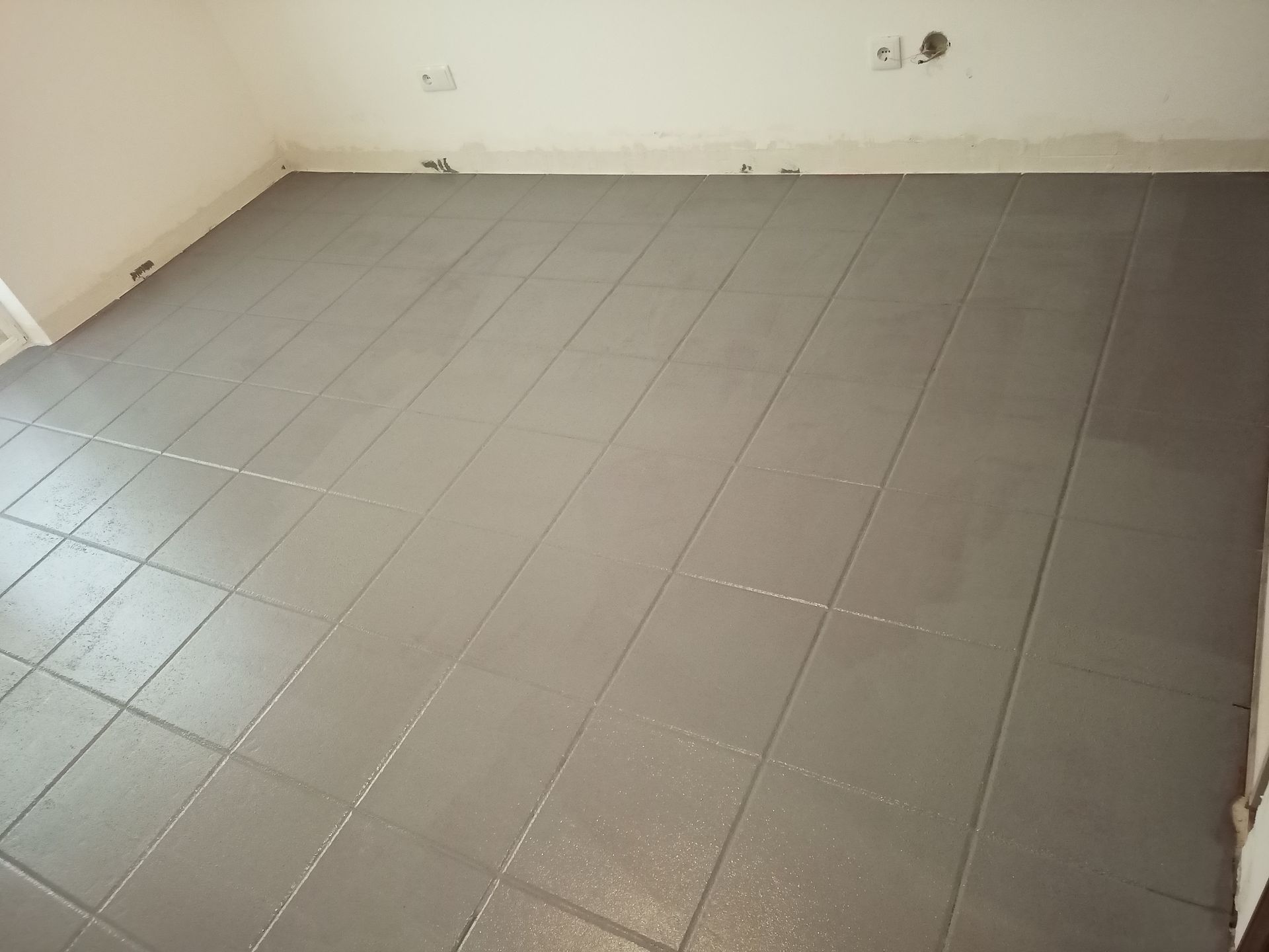 Piso cinza sendo instalado em um cômodo, apresentando um padrão quadriculado.