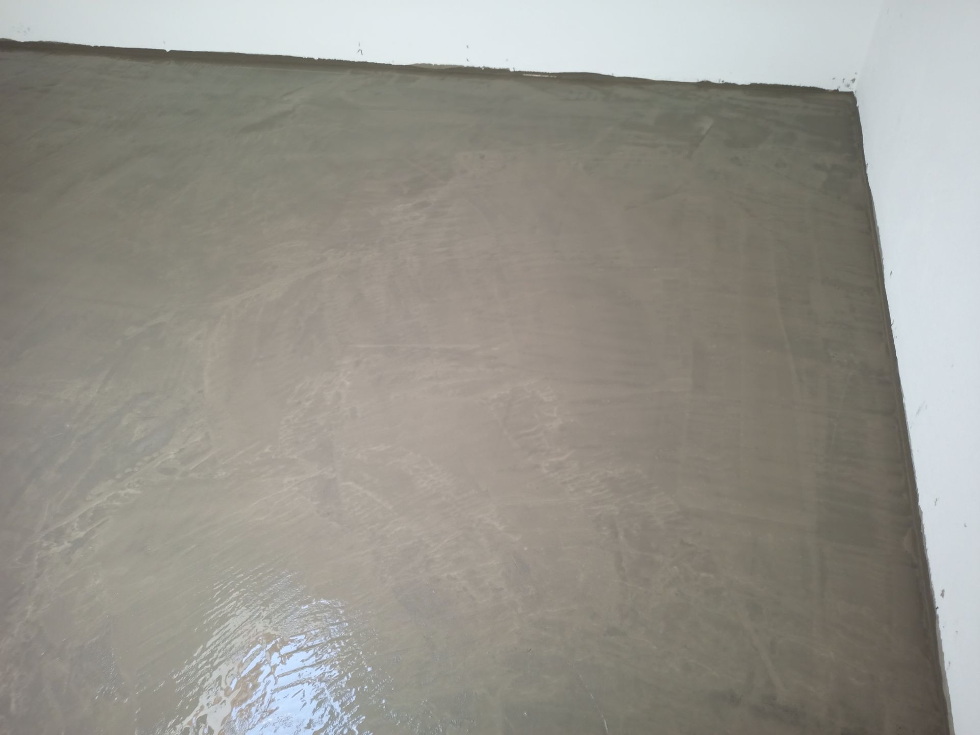 Piso de concreto cinza, recém-colocado, em uma sala adjacente a paredes brancas.