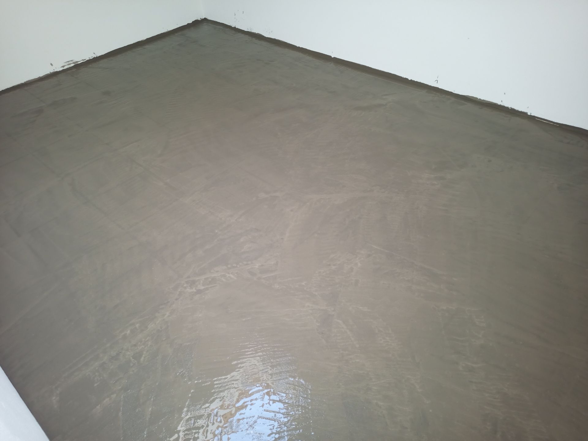 Piso de concreto cinza recém-moldado em um canto da sala, refletindo a luz.