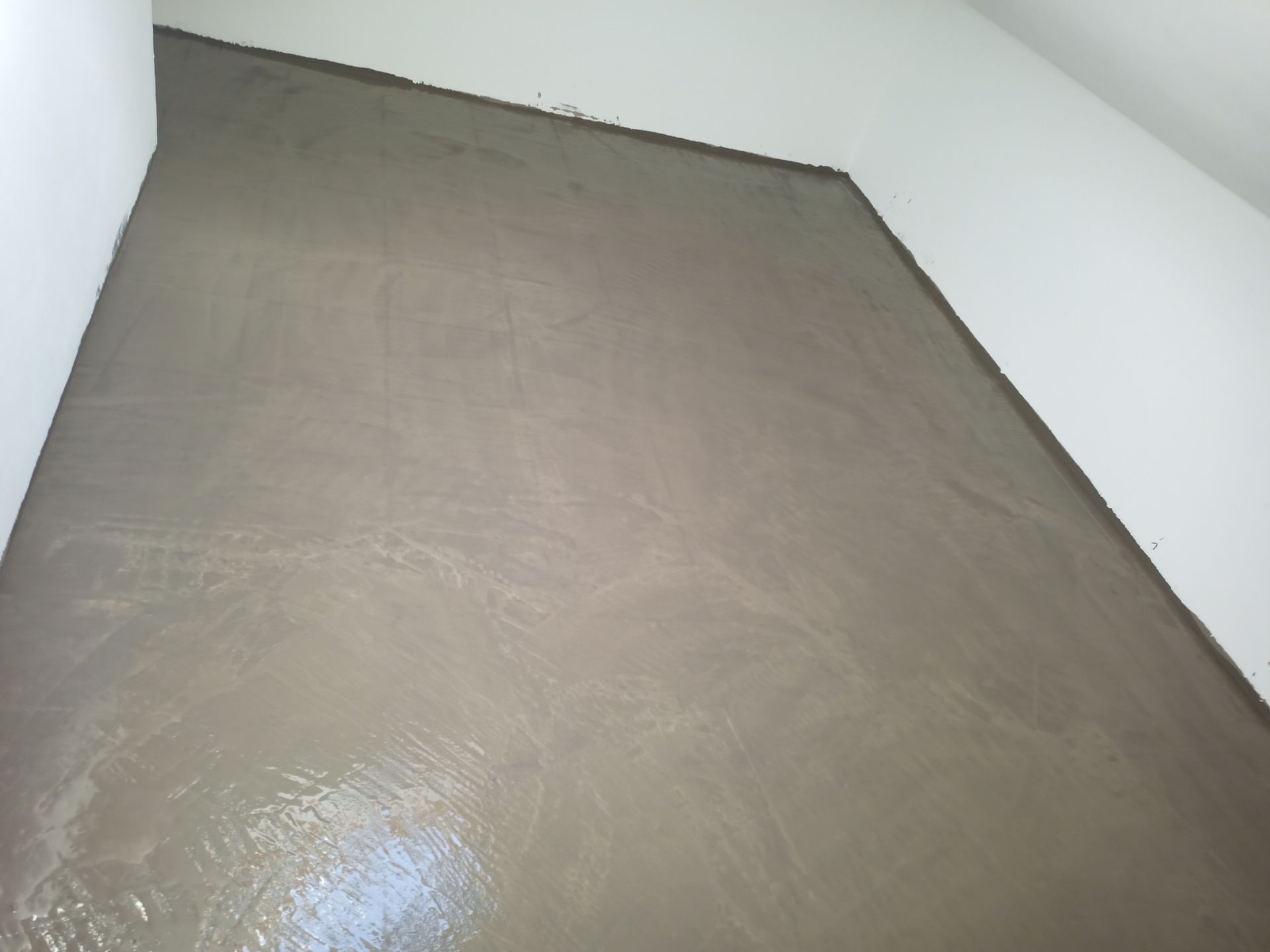 Piso de concreto fresco e úmido em um cômodo, com paredes brancas visíveis.