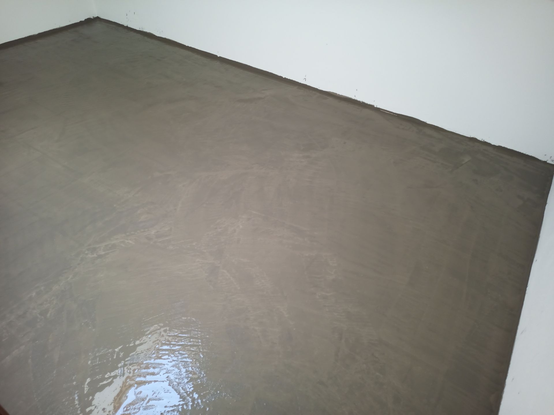 Um cômodo com piso de concreto cinza, liso e recém-colocado. Paredes brancas.