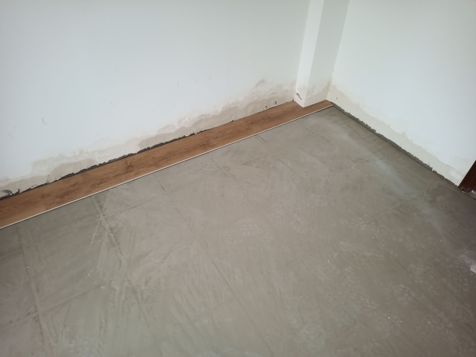 Canto de um quarto com piso de concreto cinza e molhado e paredes brancas.