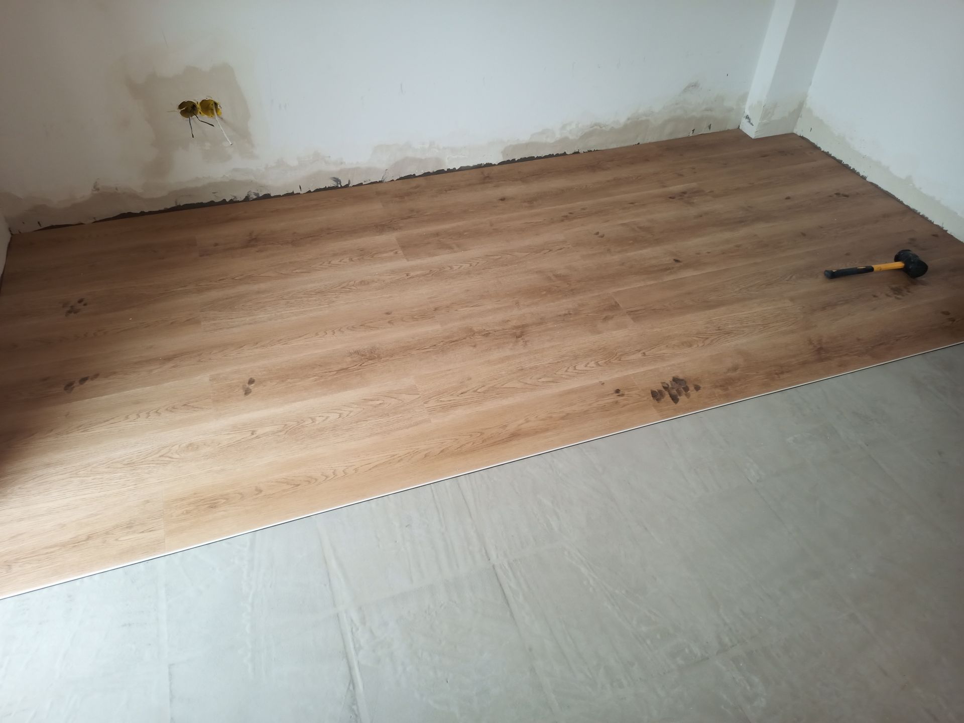 Piso com aparência de madeira sendo instalado em um cômodo. Um martelo está sobre o piso parcialmente revestido.