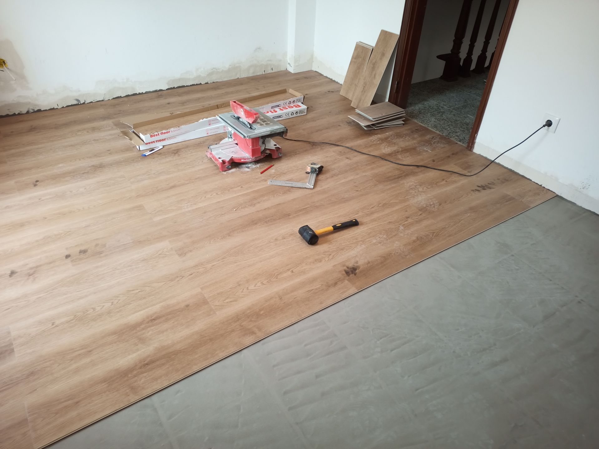 Instalação de piso laminado de madeira em um cômodo; ferramentas e materiais estão espalhados.