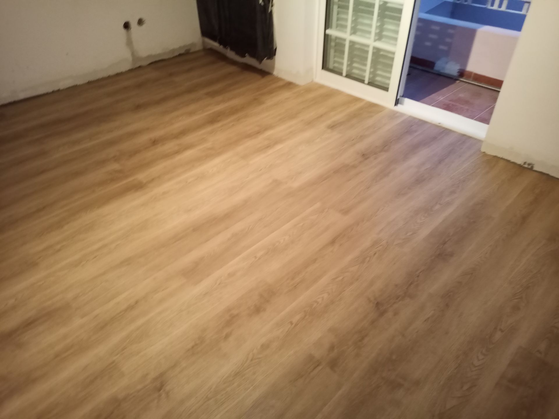 Piso de madeira em um quarto com uma porta branca fechada que dá para uma varanda.