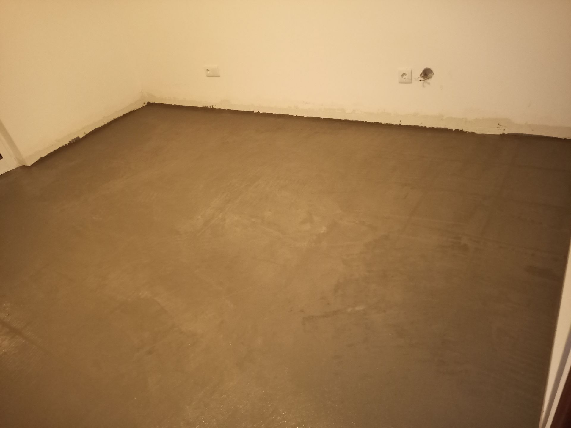 Quarto com piso de concreto novo, de cor marrom claro, contra paredes brancas.