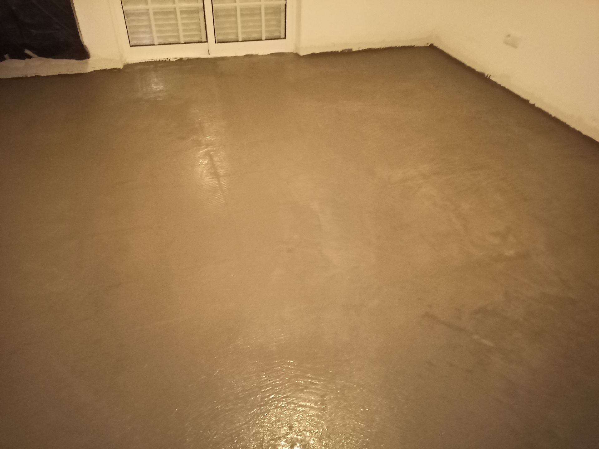 Um piso de cimento cinza, liso e recém-colocado, em uma sala, refletindo a luz.